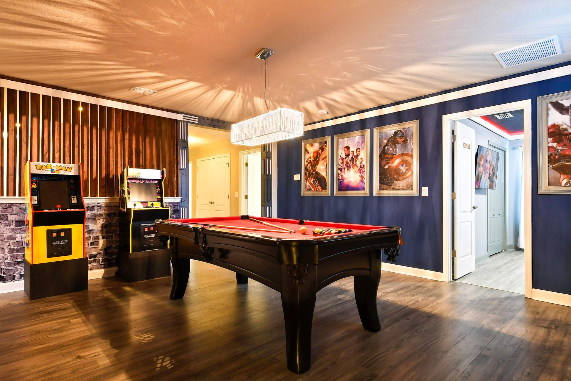 Game room with a pool table, classic arcade machines, and Marvel superhero posters on navy blue walls.