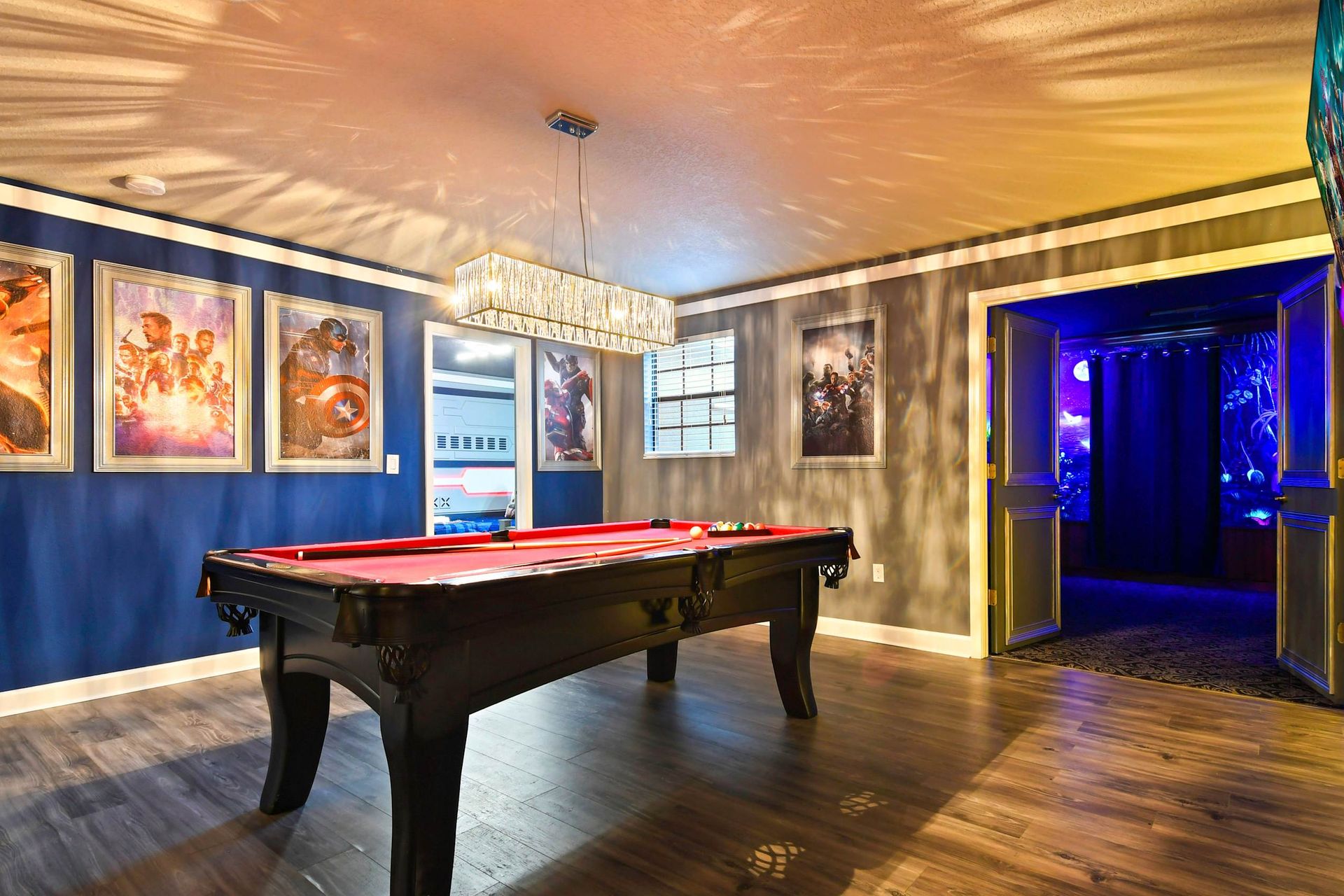 Stylish game room with pool table, Marvel posters, and adjoining theater with glowing purple lights.