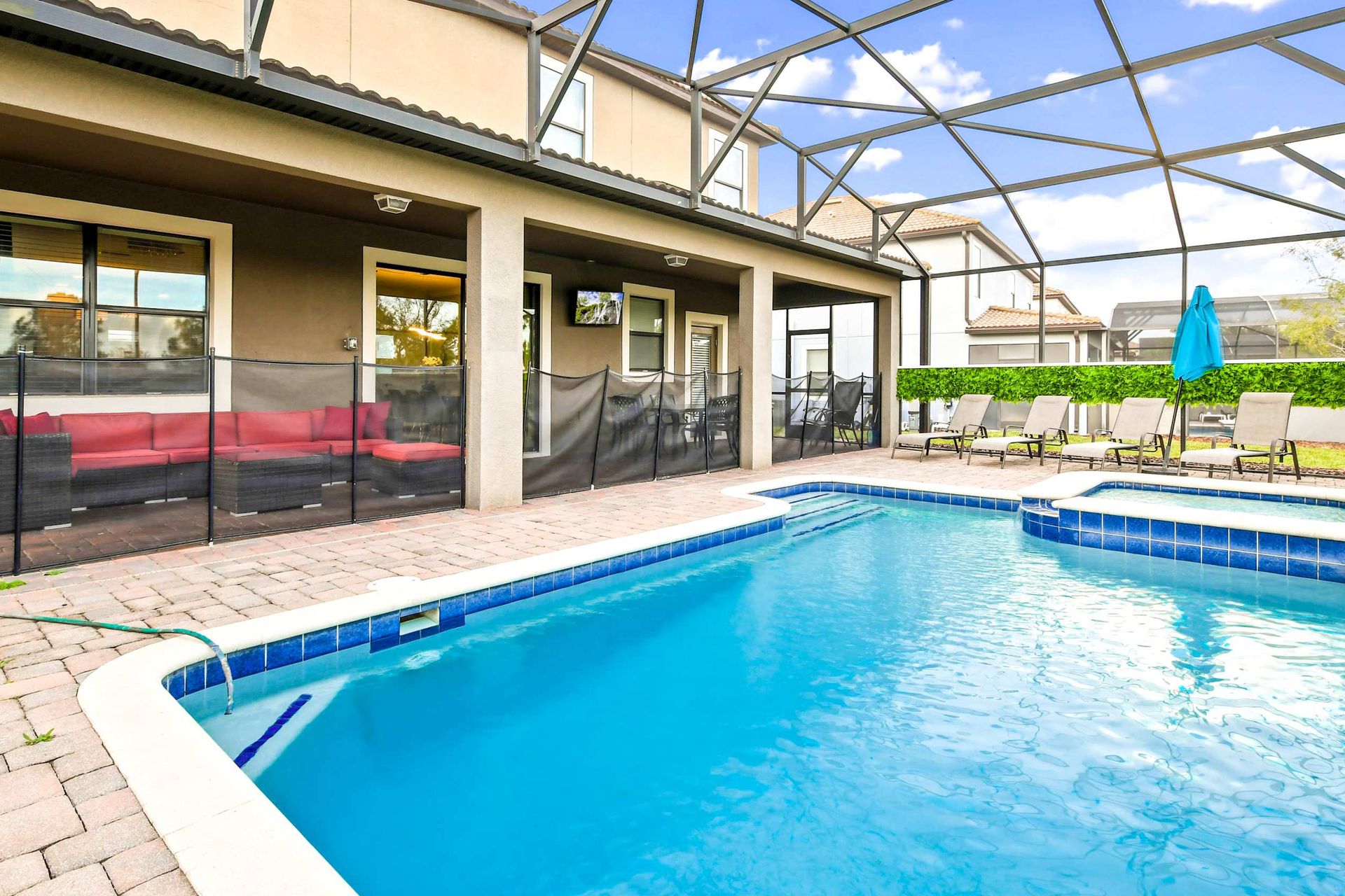 Inviting patio with pool, hot tub, lounge chairs, and a cozy red sectional, perfect for relaxation.