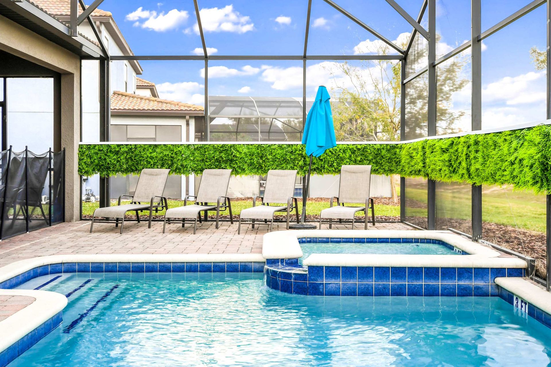 Luxurious screened-in patio with blue pool, hot tub, lounge chairs, and greenery for ultimate relaxation.