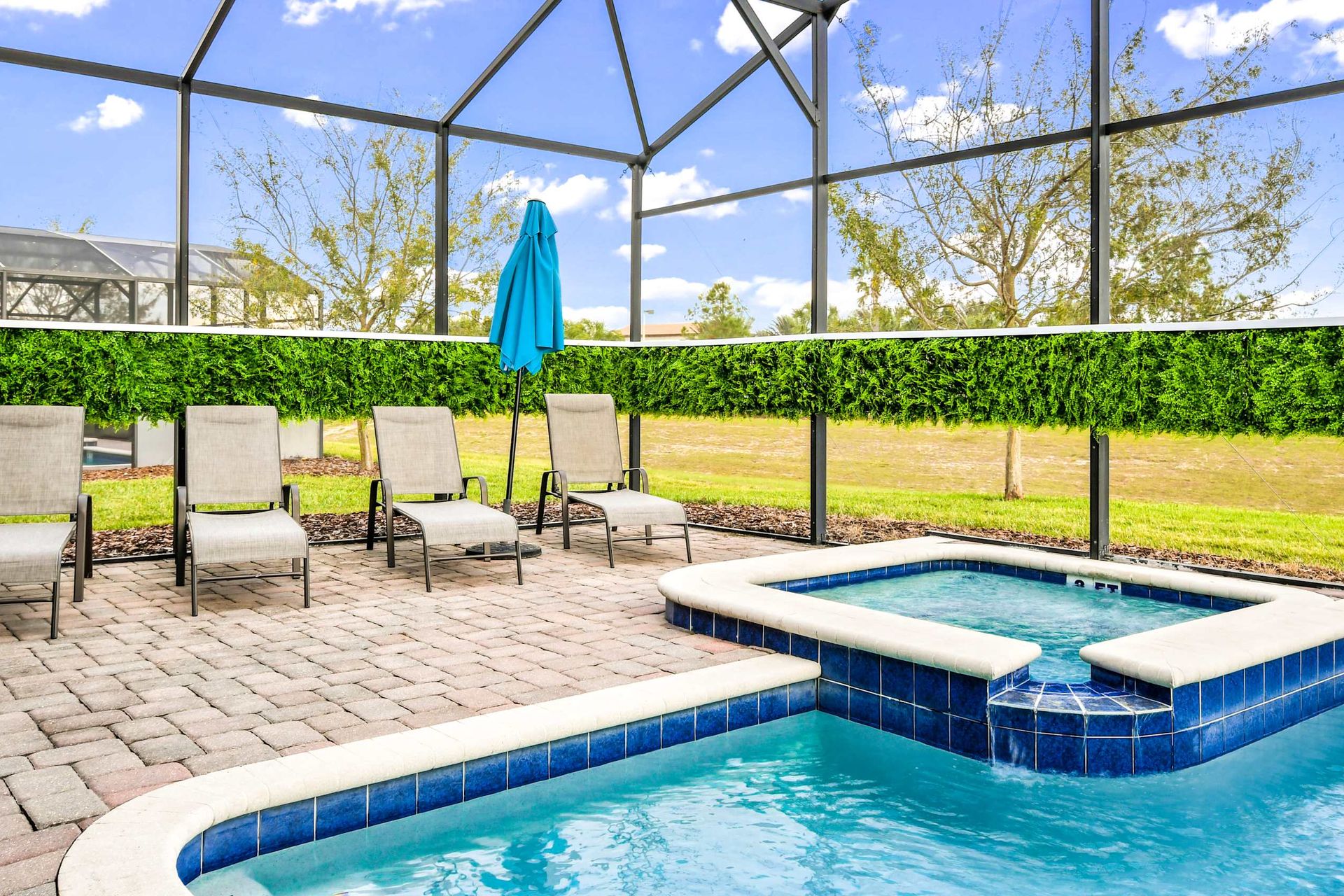 Inviting pool area with lush greenery, comfy loungers, and a hot tub under a clear blue sky.