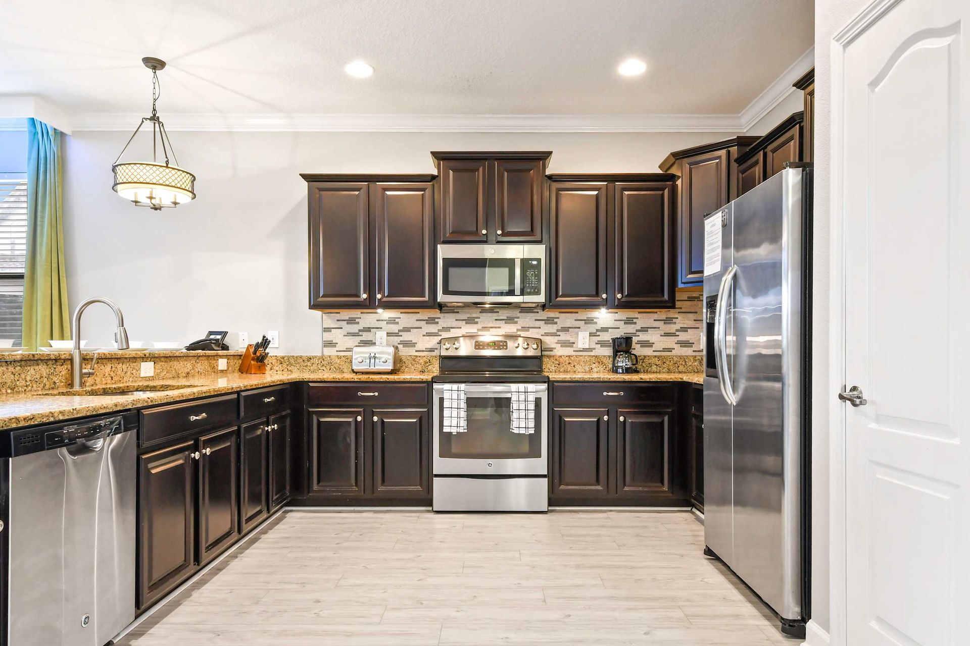 Sleek kitchen with dark wood cabinets, stainless steel appliances, granite countertops, and modern lighting.