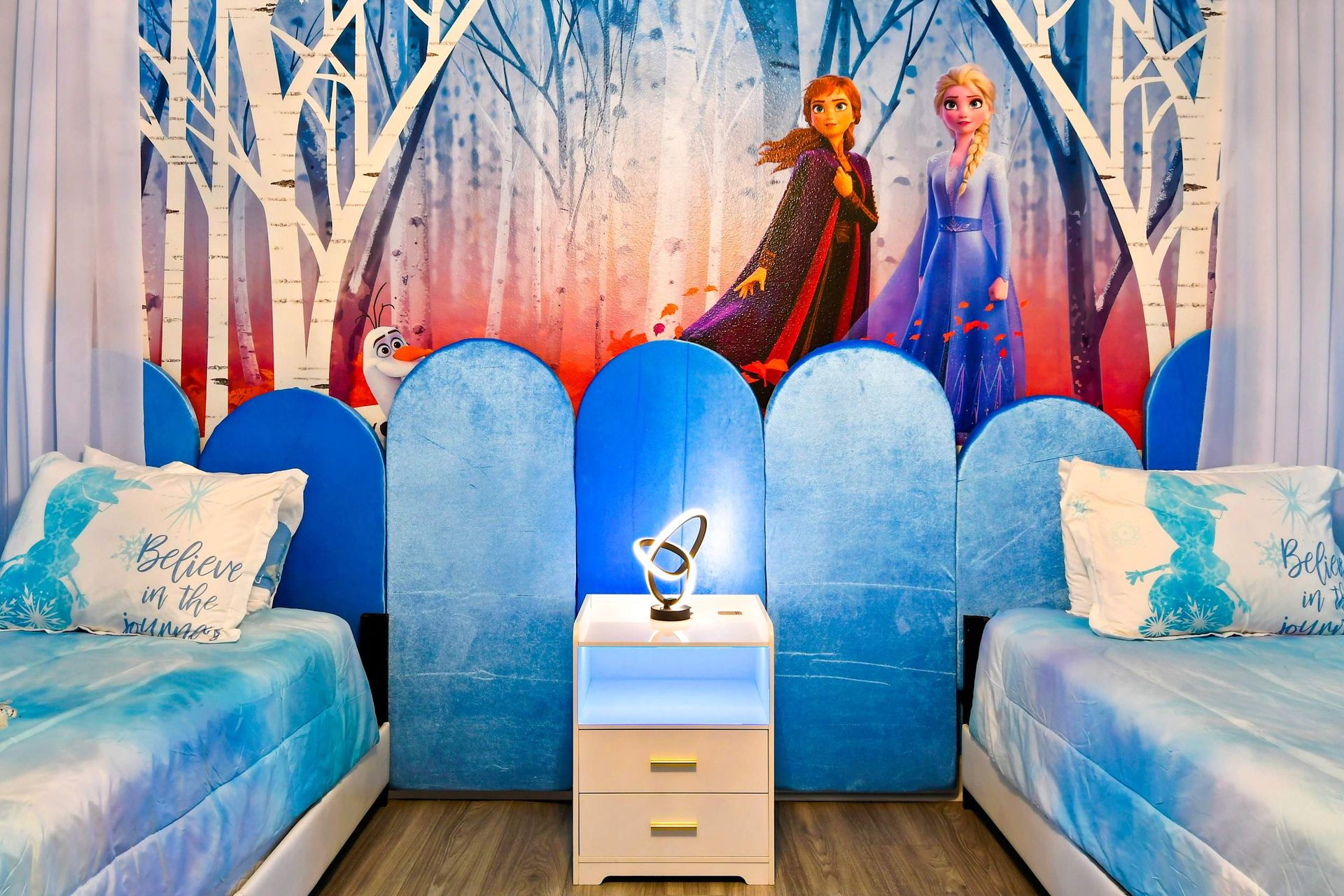 Frozen-themed bedroom with twin beds, featuring Elsa and Anna bedding, a snowy forest mural, and Olaf pillows.