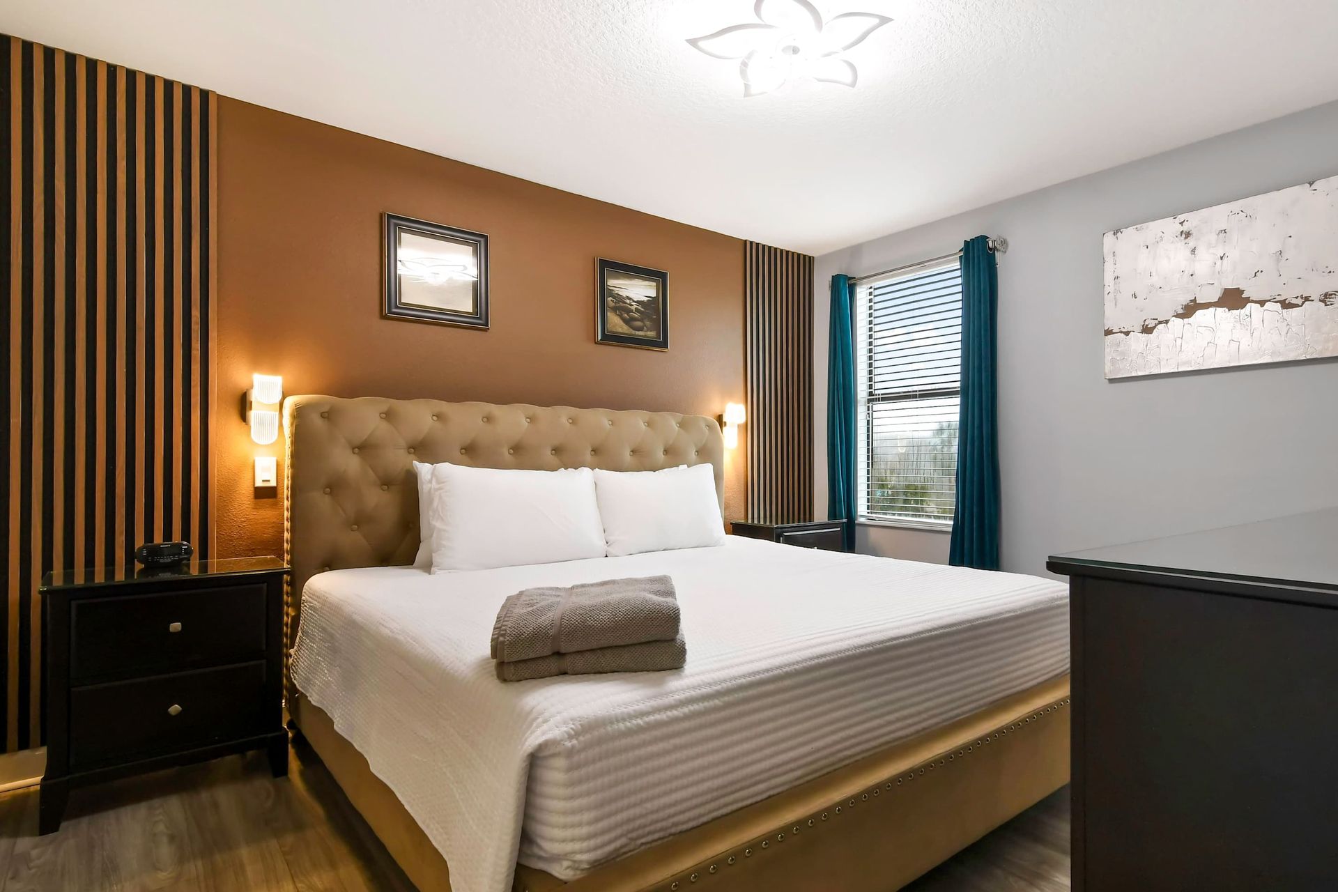Elegant bedroom with a tufted bed, cozy lighting, dark wood accents, and modern wall art.