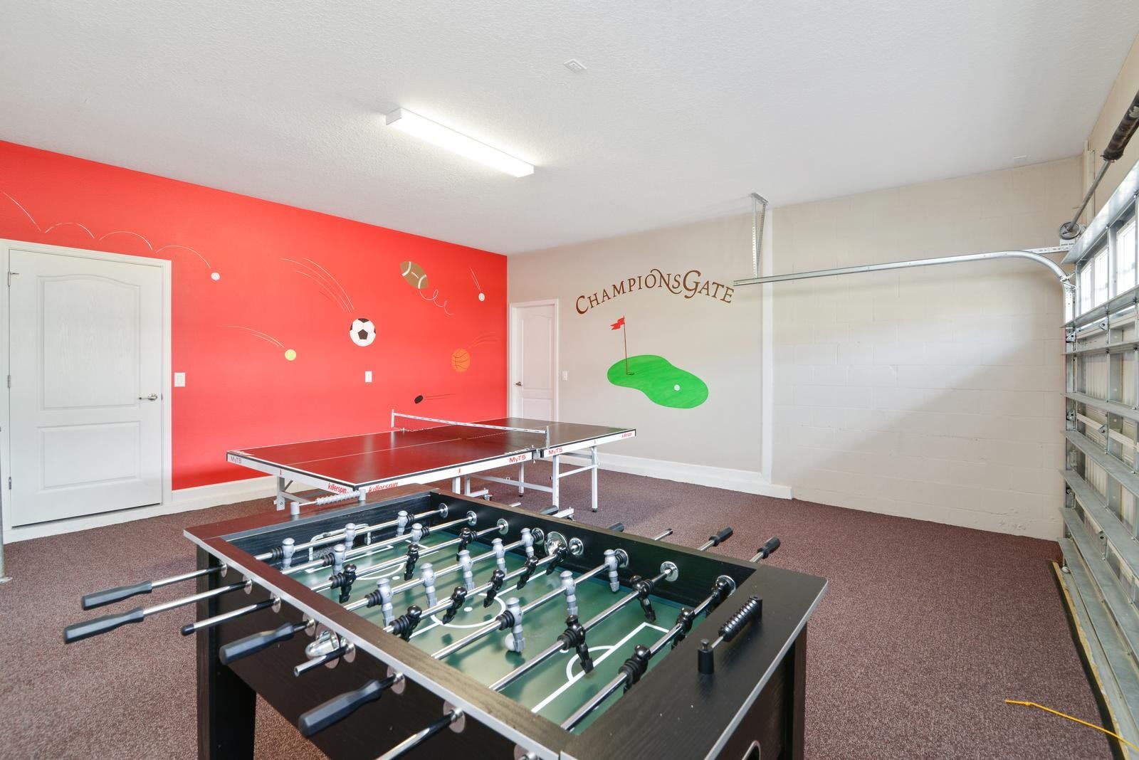 Bright game room with a foosball table, ping pong table, sports-themed wall art, and ample lighting.