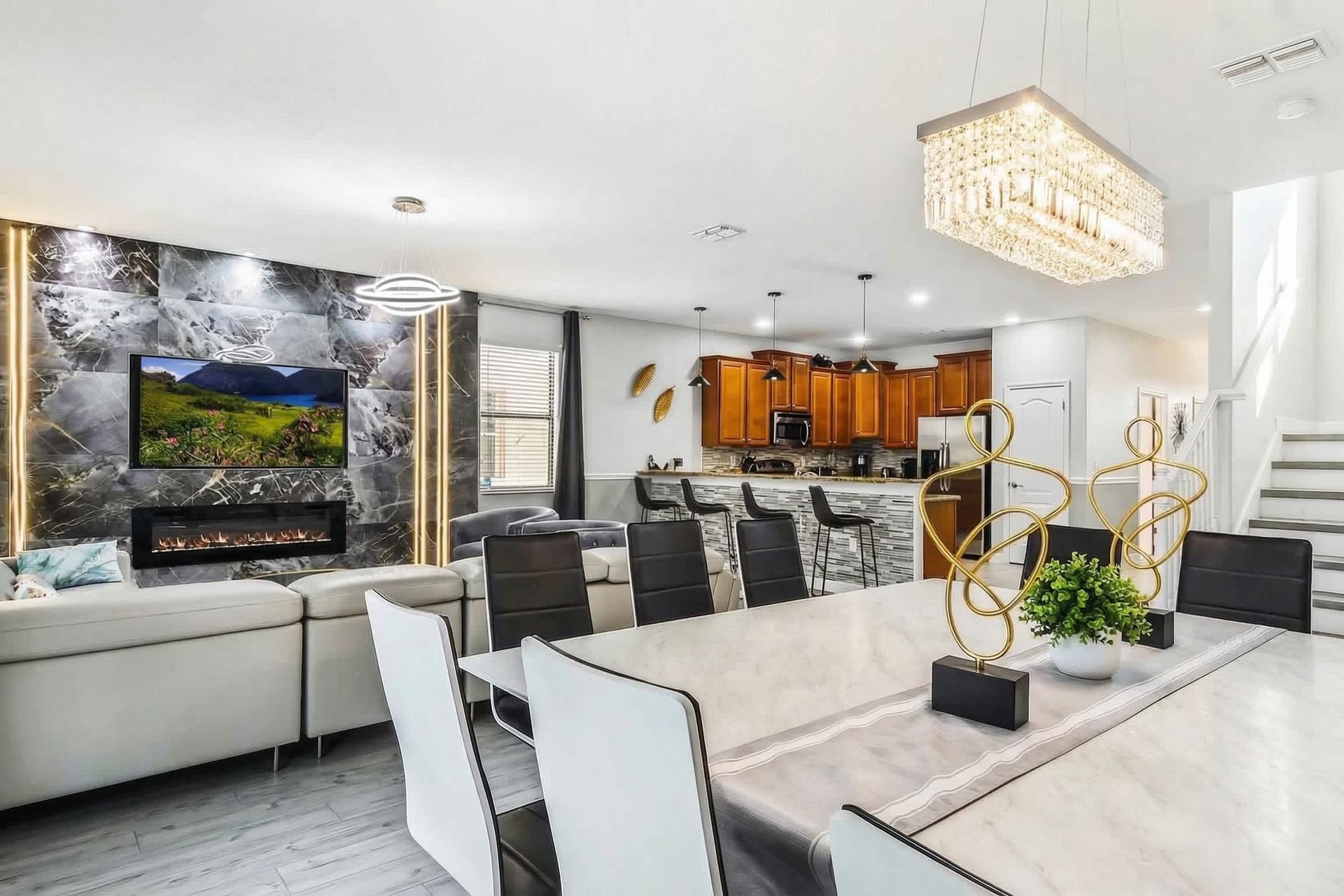 Elegant open-concept living area with a modern fireplace, marble accents, crystal chandelier, and a stylish kitchen.