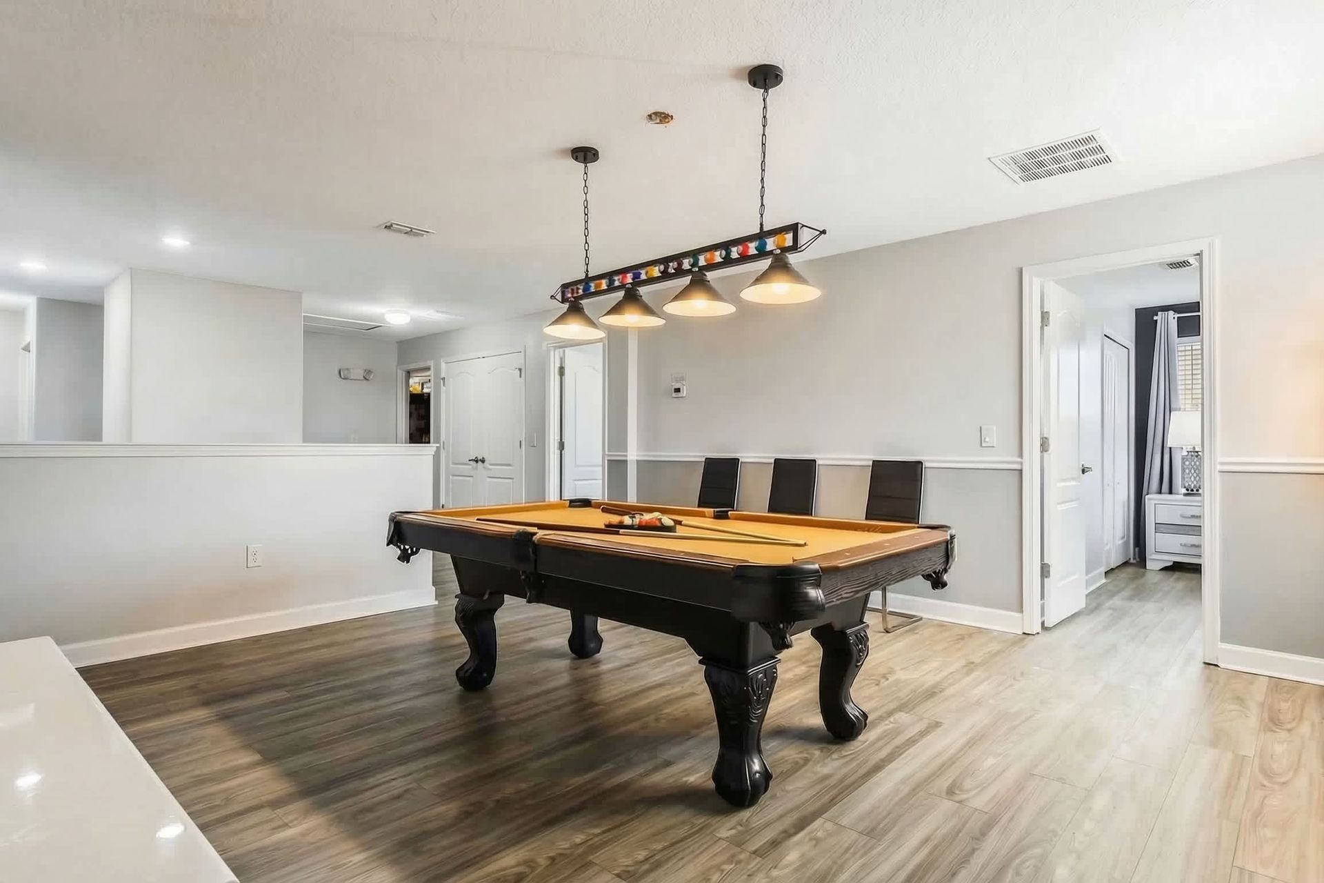 Stylish game room with a sleek pool table, modern lighting, and minimalist decor on wood laminate flooring.