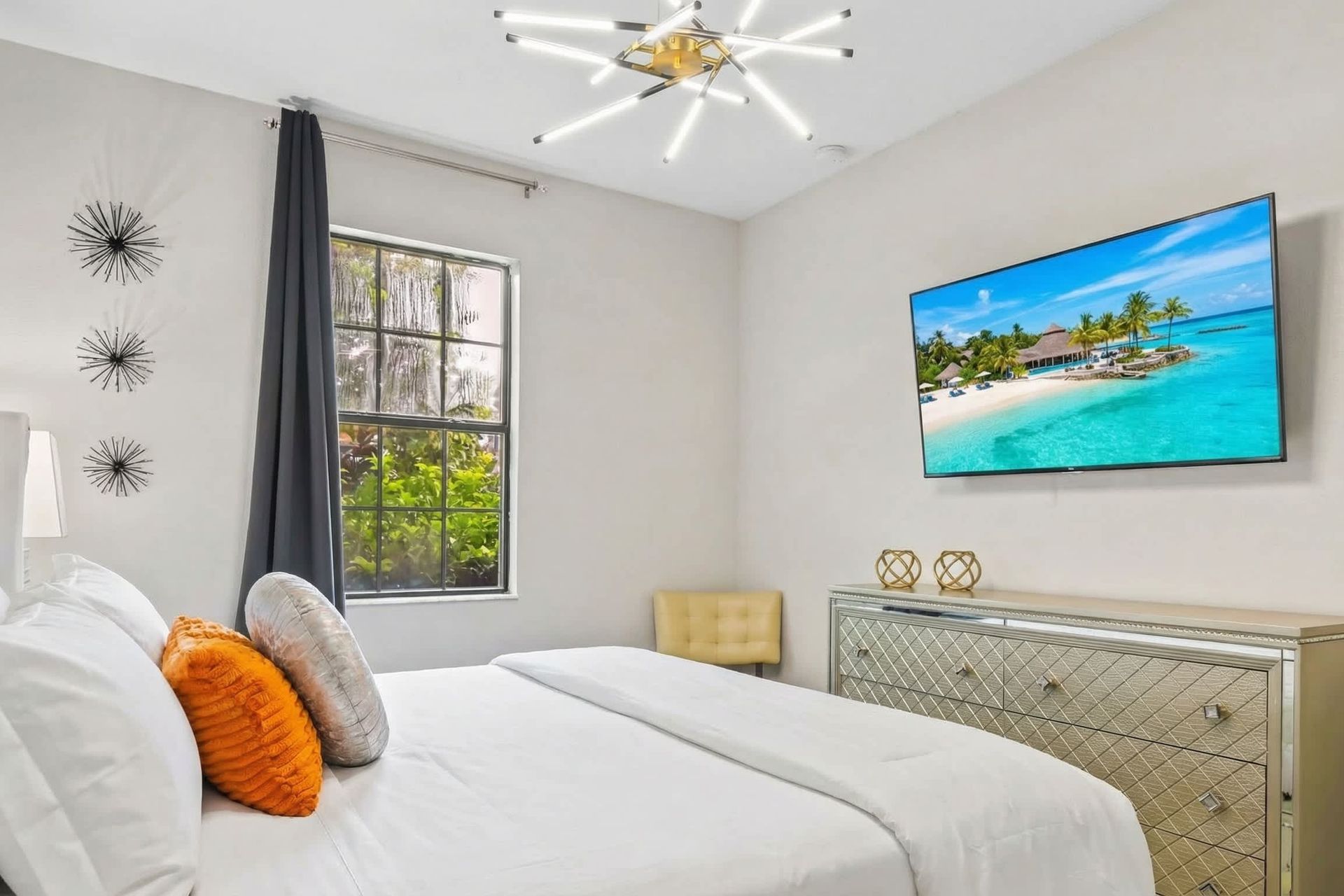 Modern bedroom with chic decor, featuring a stylish bed with textured bedding, a unique chandelier, and a wall-mounted TV.