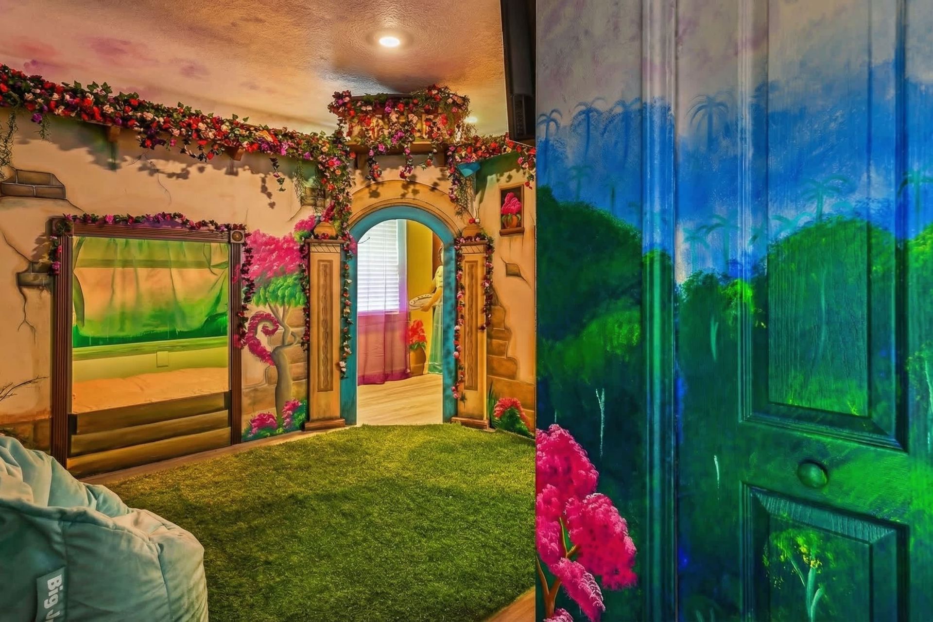 Enchanting room with a garden-themed mural, archway adorned with flowers, and a cozy bean bag on grass-like carpet.
