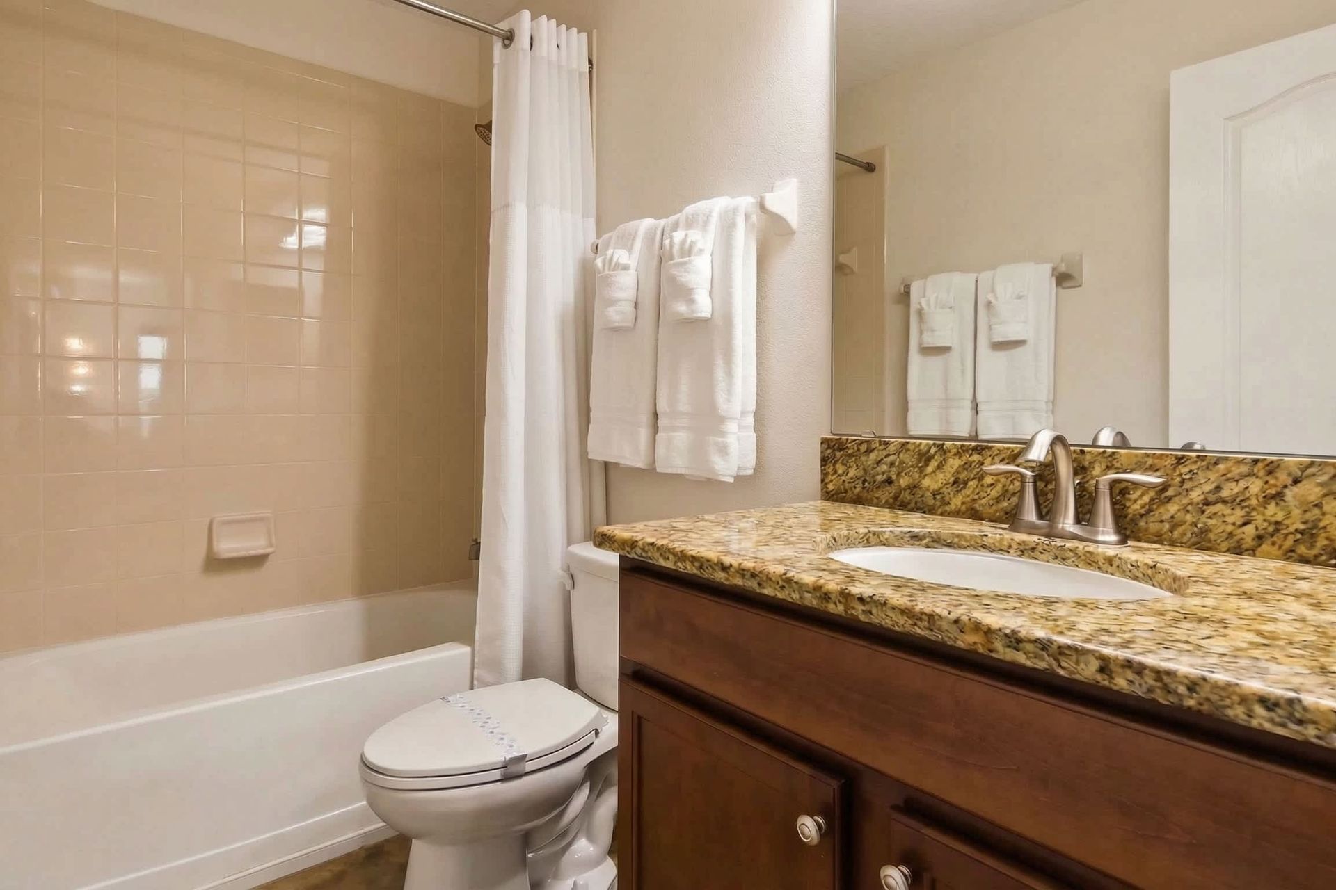 Modern bathroom with a granite countertop, wooden vanity, tiled shower-tub combo, and sleek fixtures.