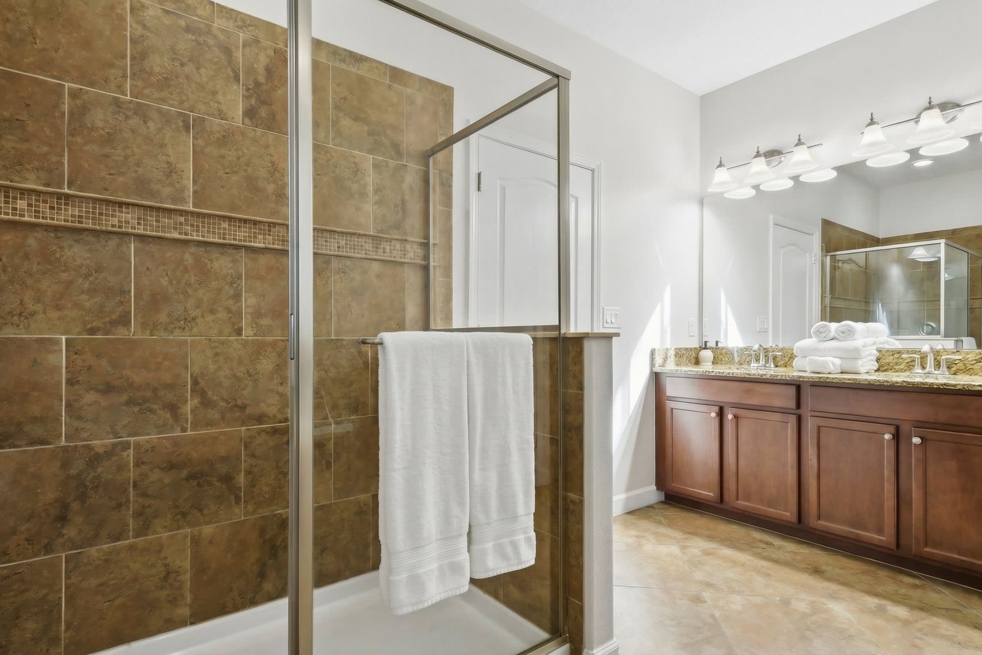 Elegant bathroom with a large walk-in shower, dual granite vanity, wooden cabinets, and modern lighting.