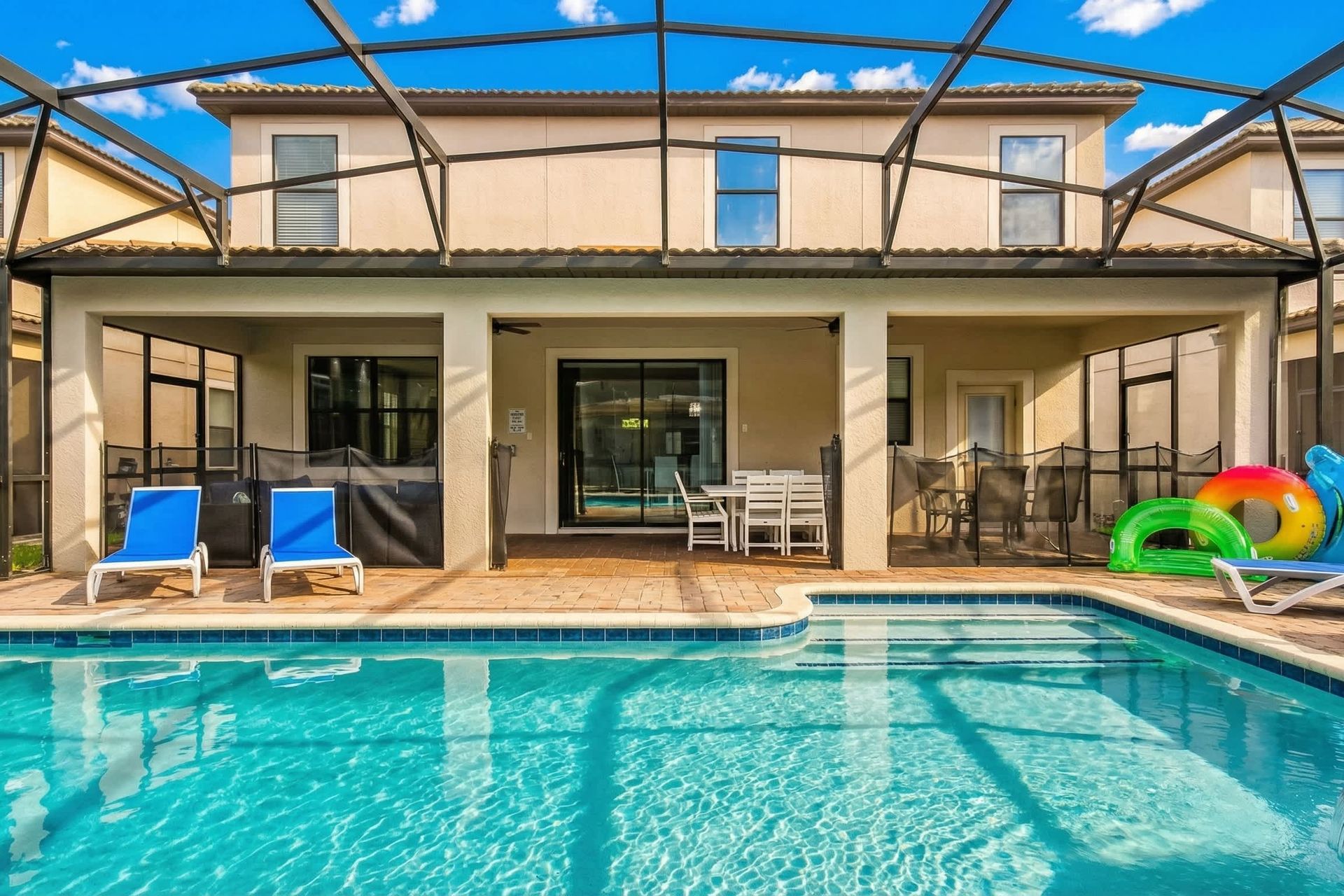 Modern backyard with a screened-in patio, refreshing pool, blue lounge chairs, and a dining area.