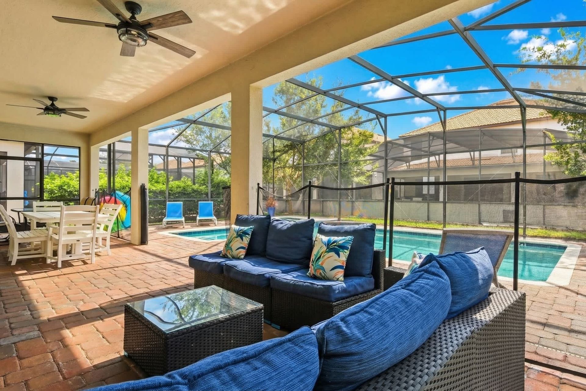 Spacious screened-in patio with cozy seating, dining area, ceiling fans, and a view of the inviting pool.
