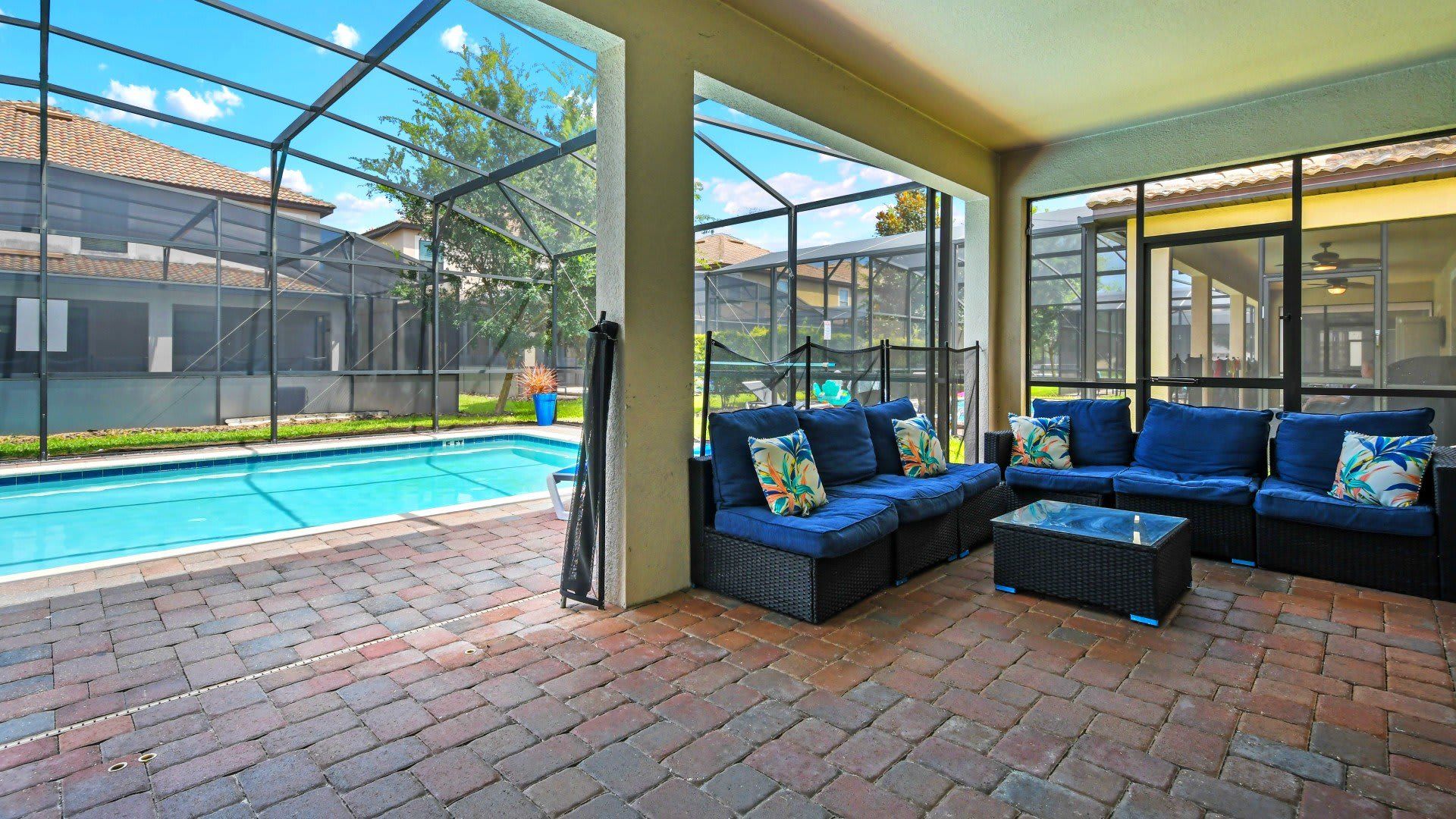 Inviting screened-in patio with comfortable blue seating, a glass-top coffee table, and a view of the pool.