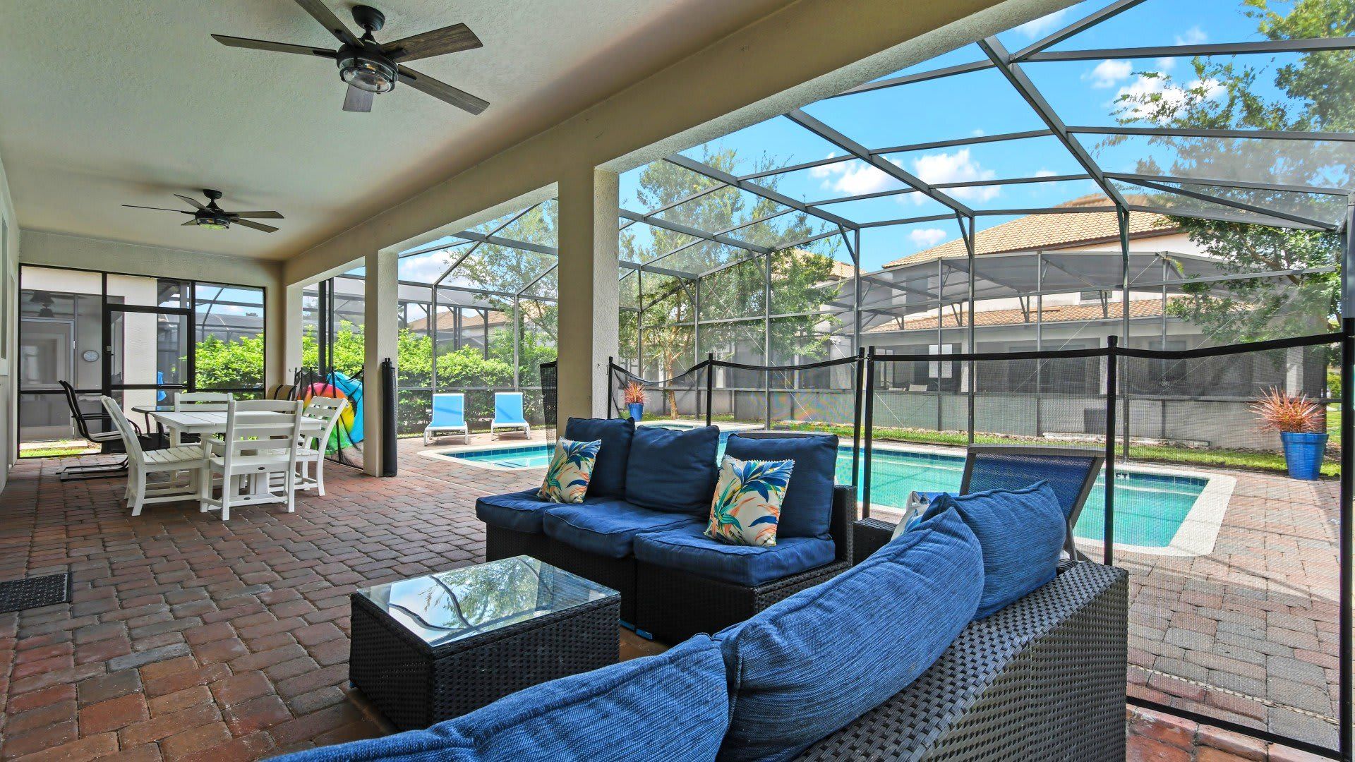 Spacious screened-in patio with cozy seating, dining area, ceiling fans, and a view of the inviting pool.