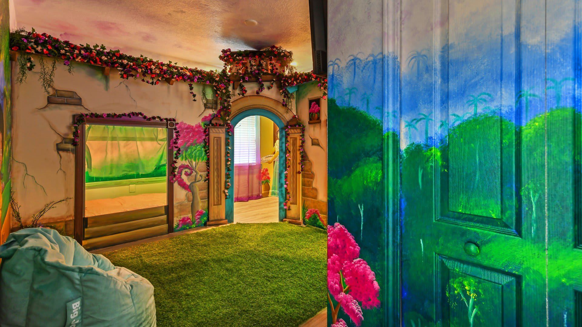 Enchanting room with a garden-themed mural, archway adorned with flowers, and a cozy bean bag on grass-like carpet.