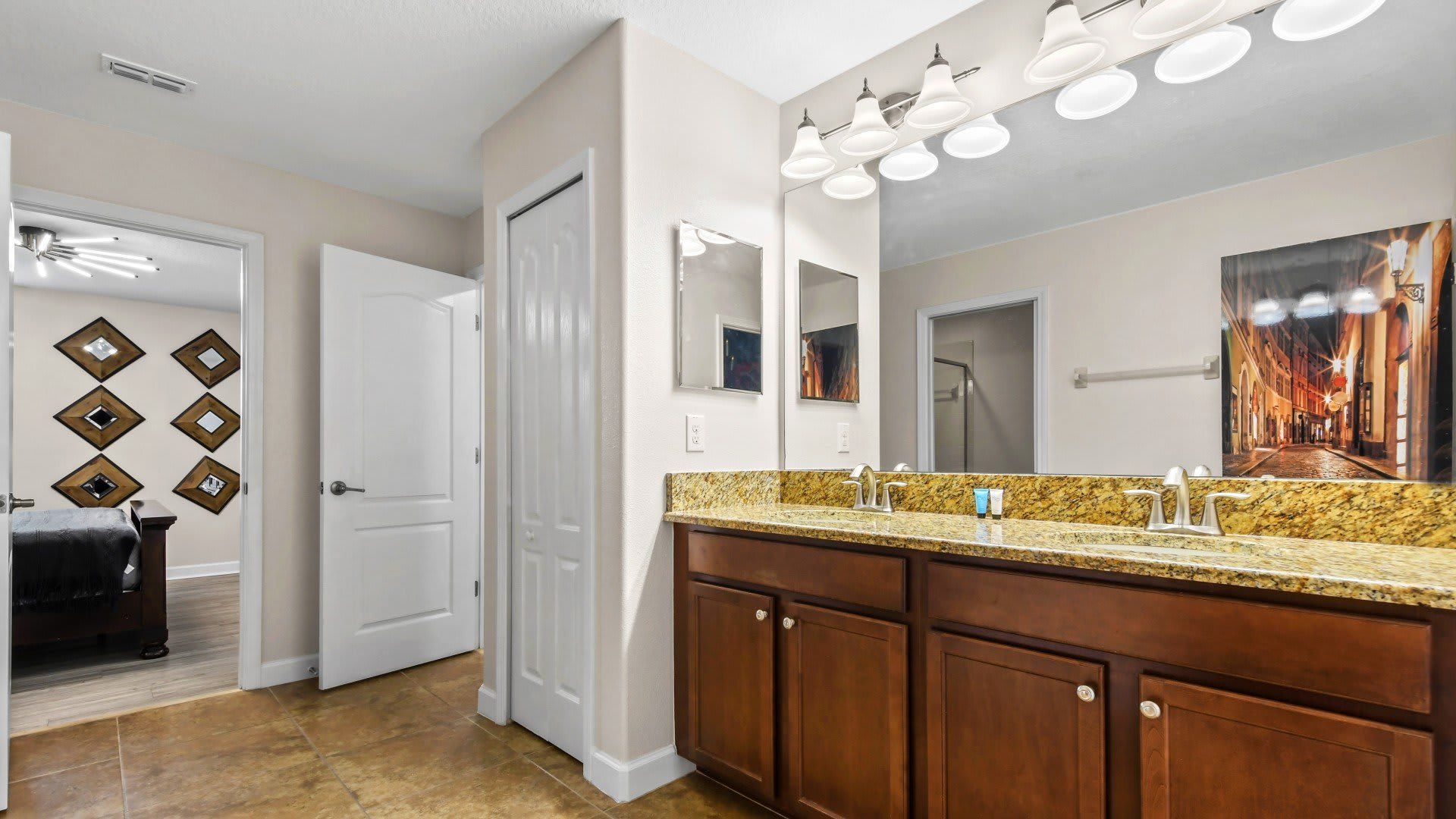Spacious bathroom with dual granite sinks, ample lighting, and an entry to a modern bedroom with chic decor.