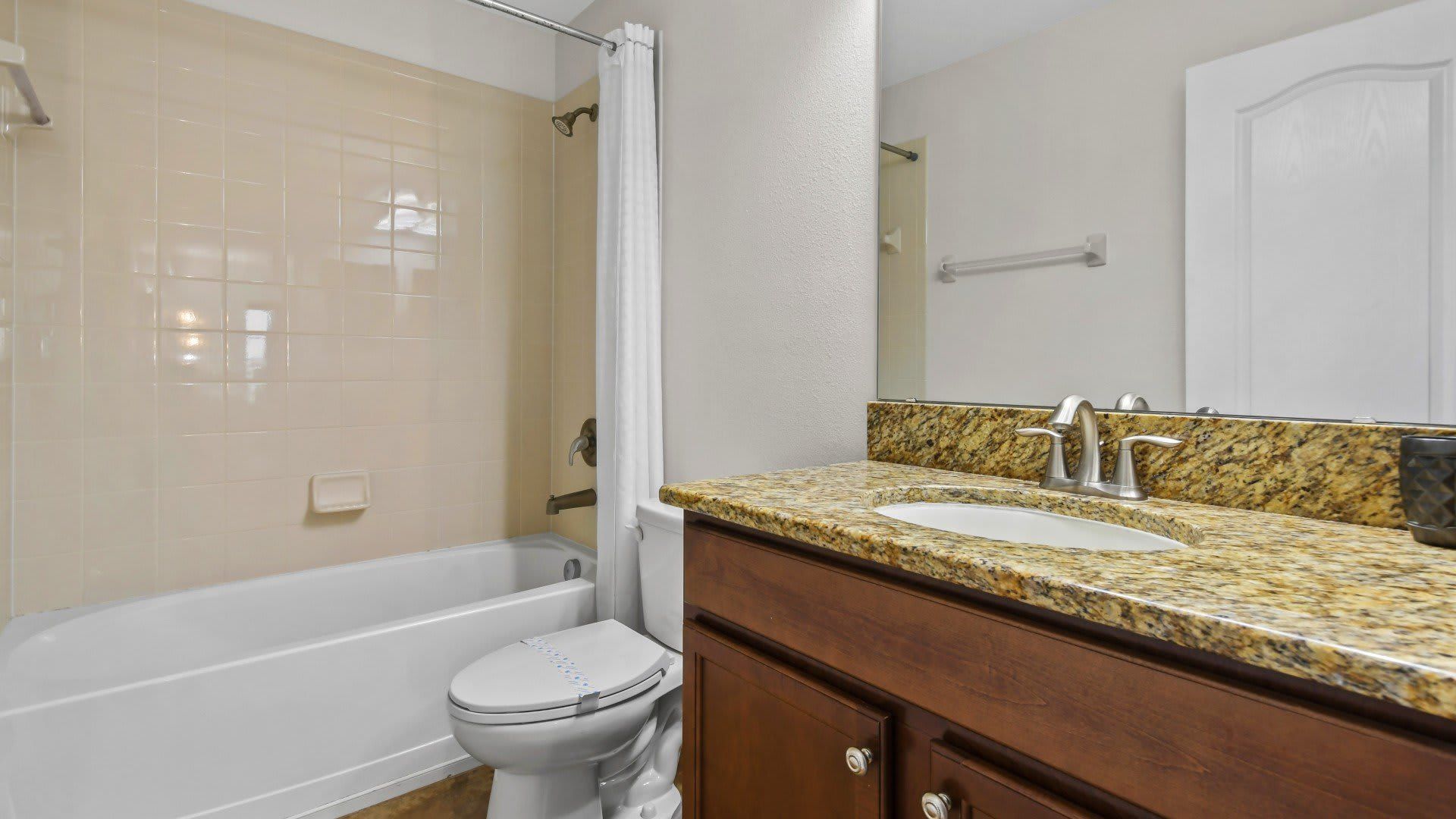 Modern bathroom with a granite countertop, wooden vanity, tiled shower-tub combo, and sleek fixtures.