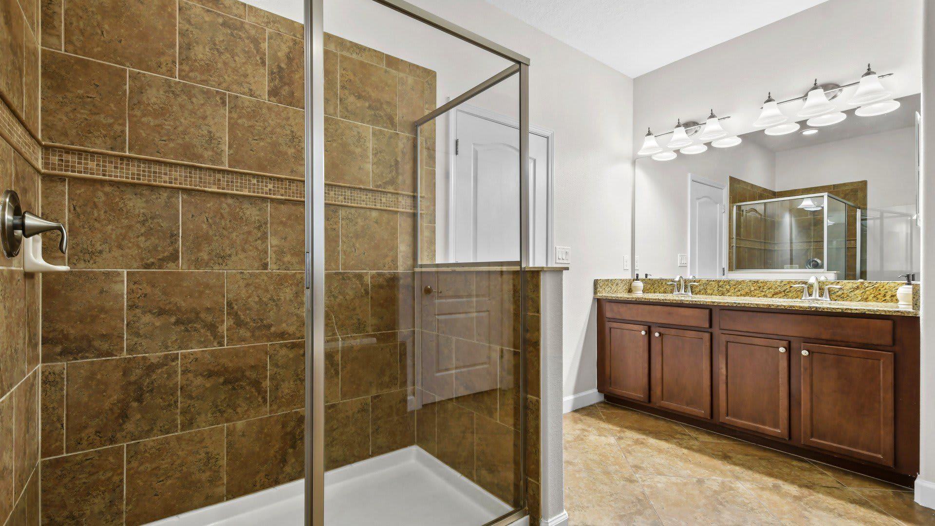 Elegant bathroom with a large walk-in shower, dual granite vanity, wooden cabinets, and modern lighting.