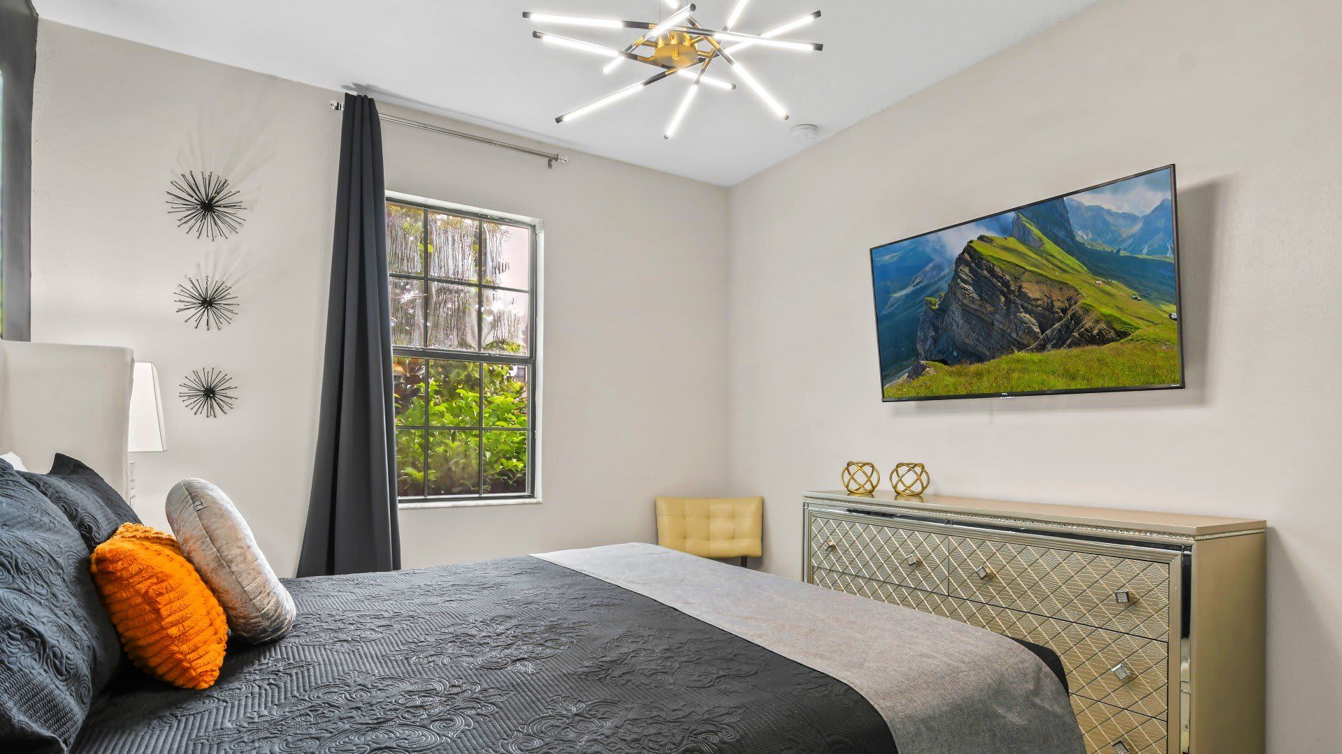 Modern bedroom with chic decor, featuring a stylish bed with textured bedding, a unique chandelier, and a wall-mounted TV.
