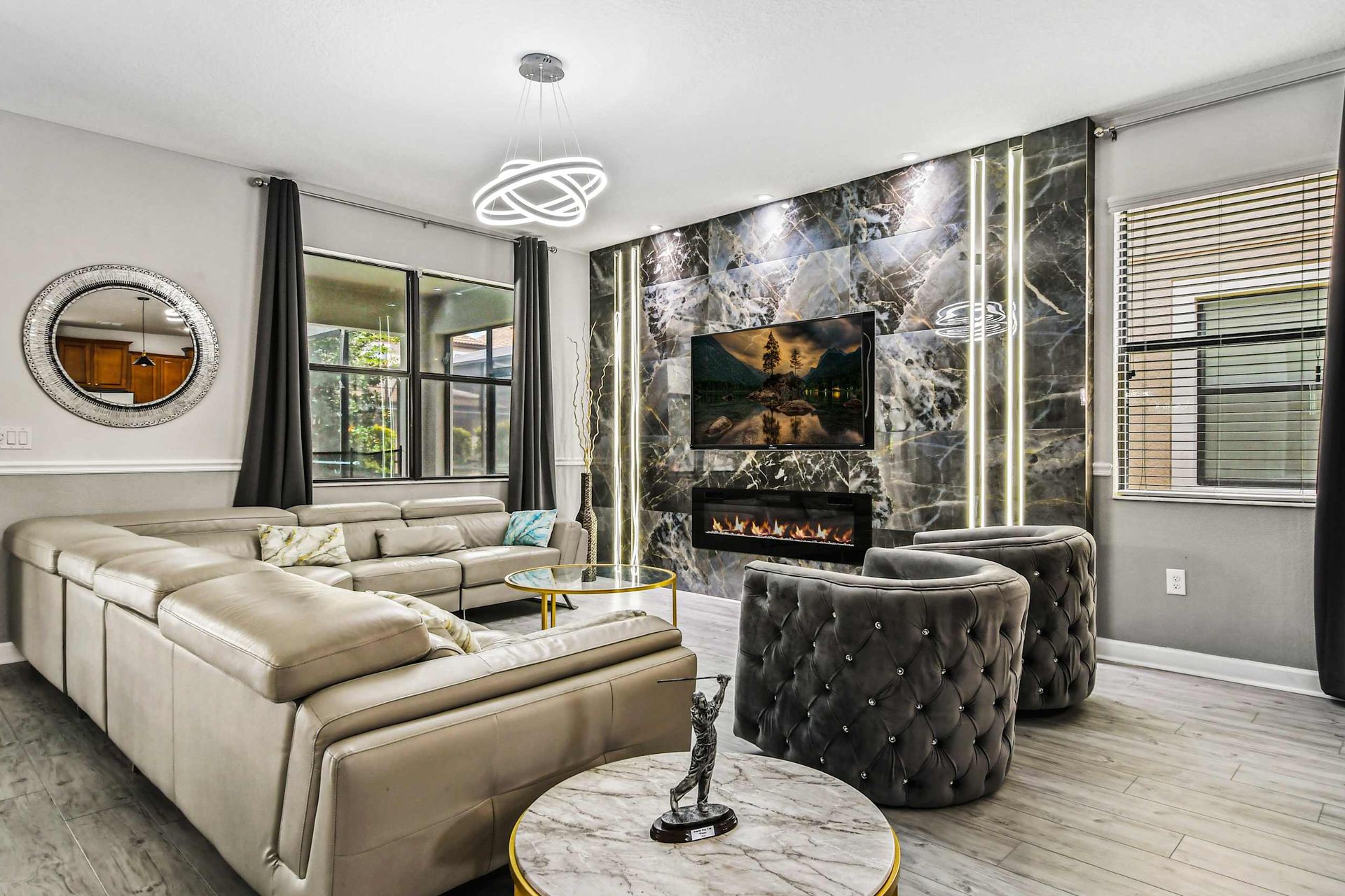 Sophisticated living room with a marble accent wall, cozy fireplace, modern chandelier, and plush seating.