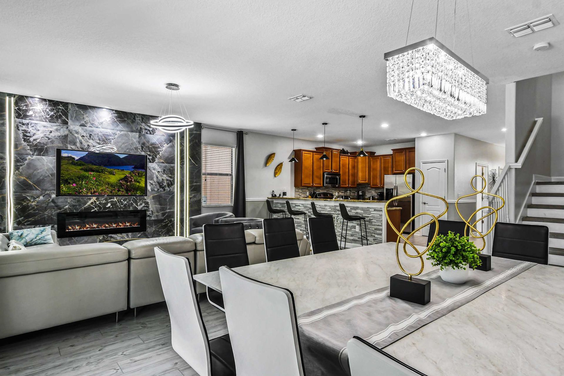 Elegant open-concept living area with a modern fireplace, marble accents, crystal chandelier, and a stylish kitchen.