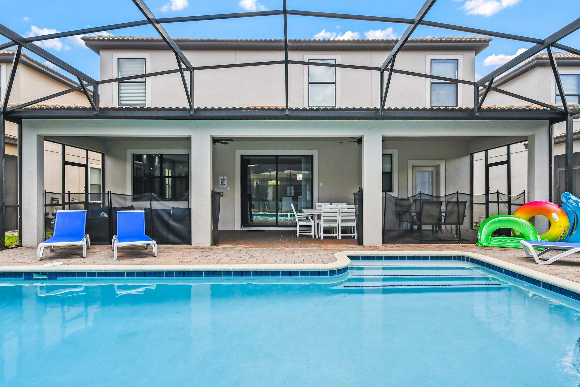 Modern backyard with a screened-in patio, refreshing pool, blue lounge chairs, and a dining area.