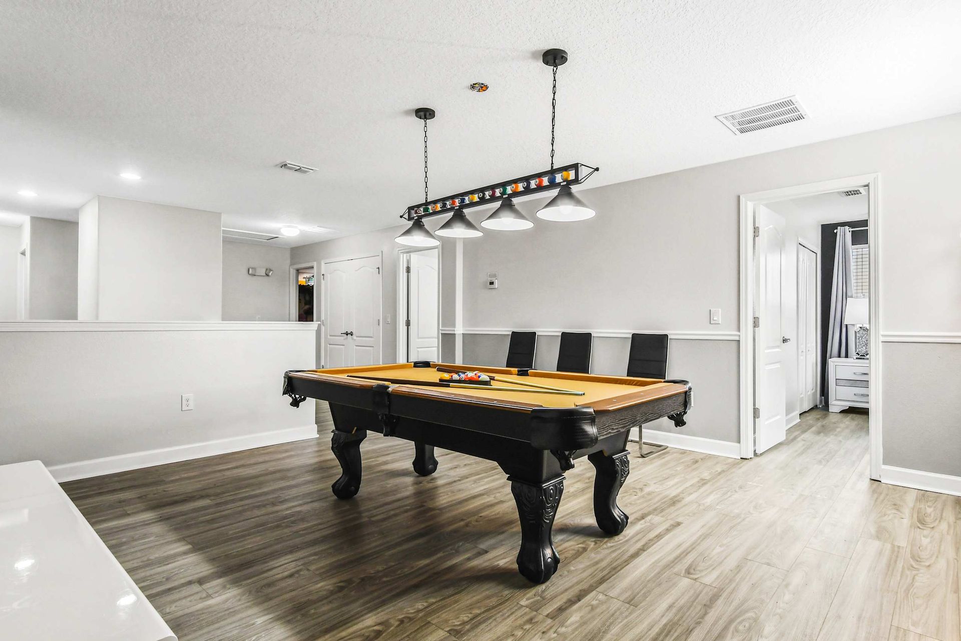 Stylish game room with a sleek pool table, modern lighting, and minimalist decor on wood laminate flooring.