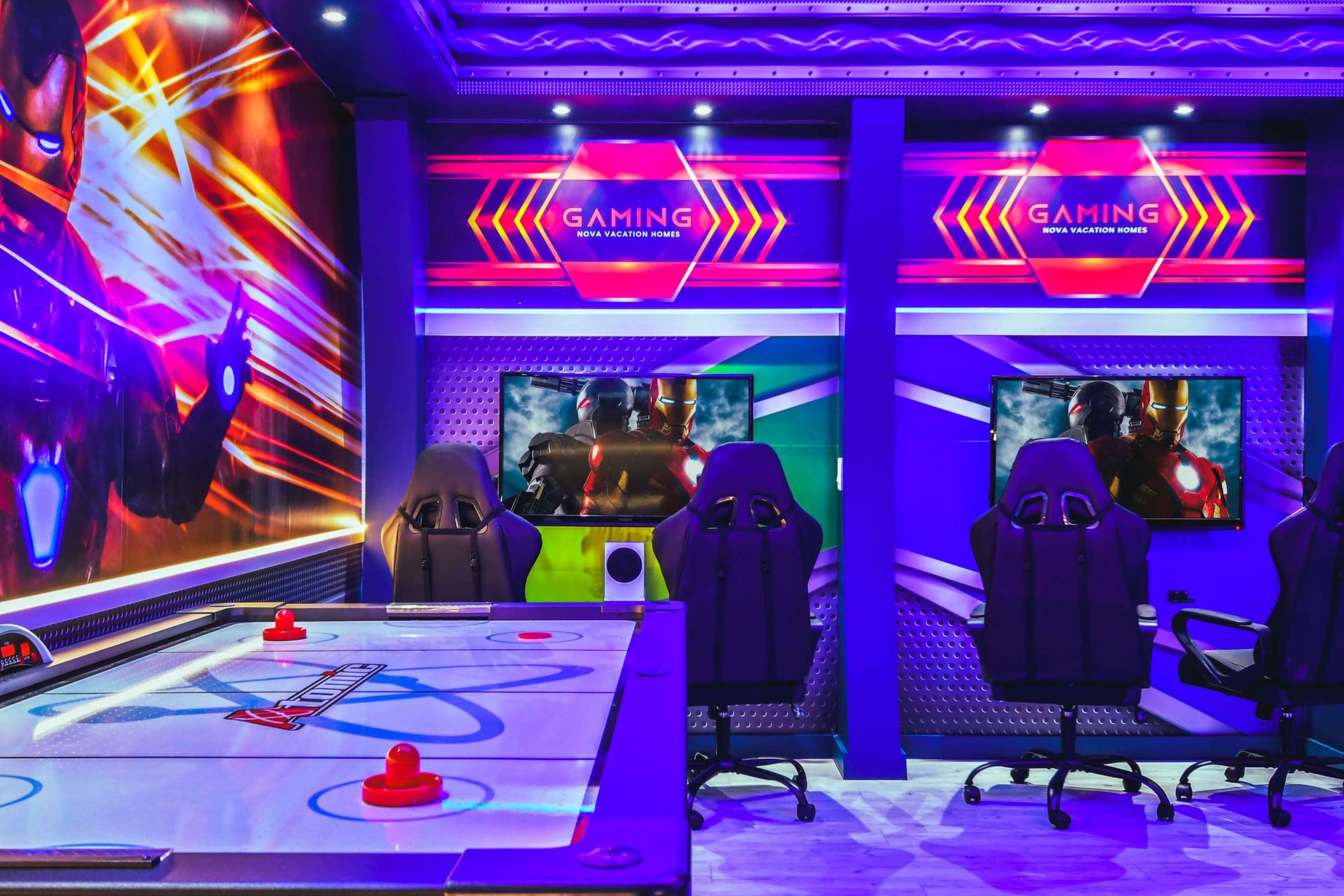 Vibrant gaming room with air hockey table, racing chairs, multiple screens, and superhero-themed decor.