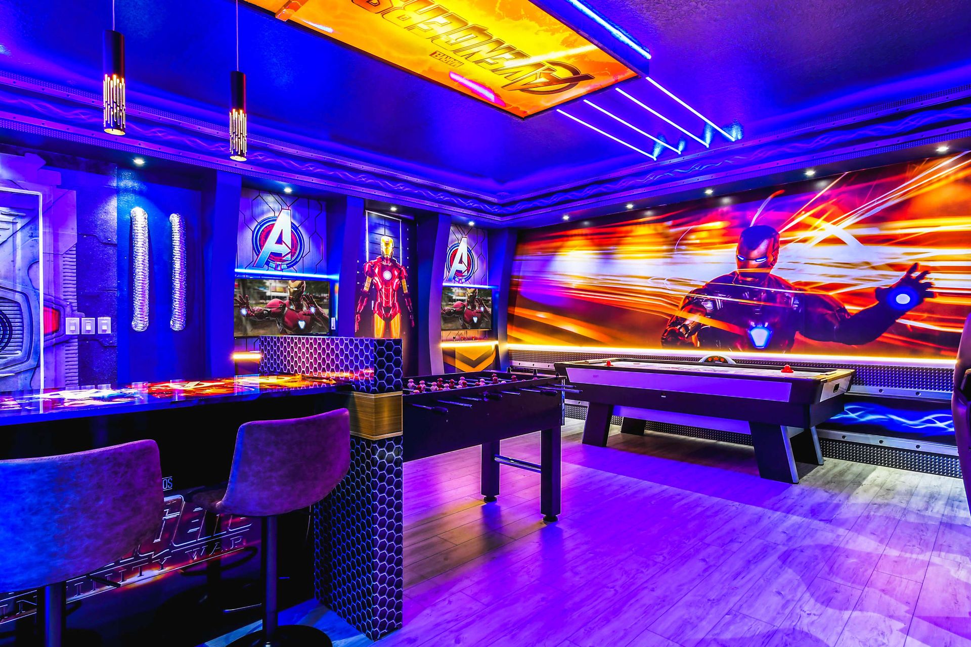 Avengers-themed game room with arcade games, air hockey, foosball, vibrant lighting, and superhero decor.