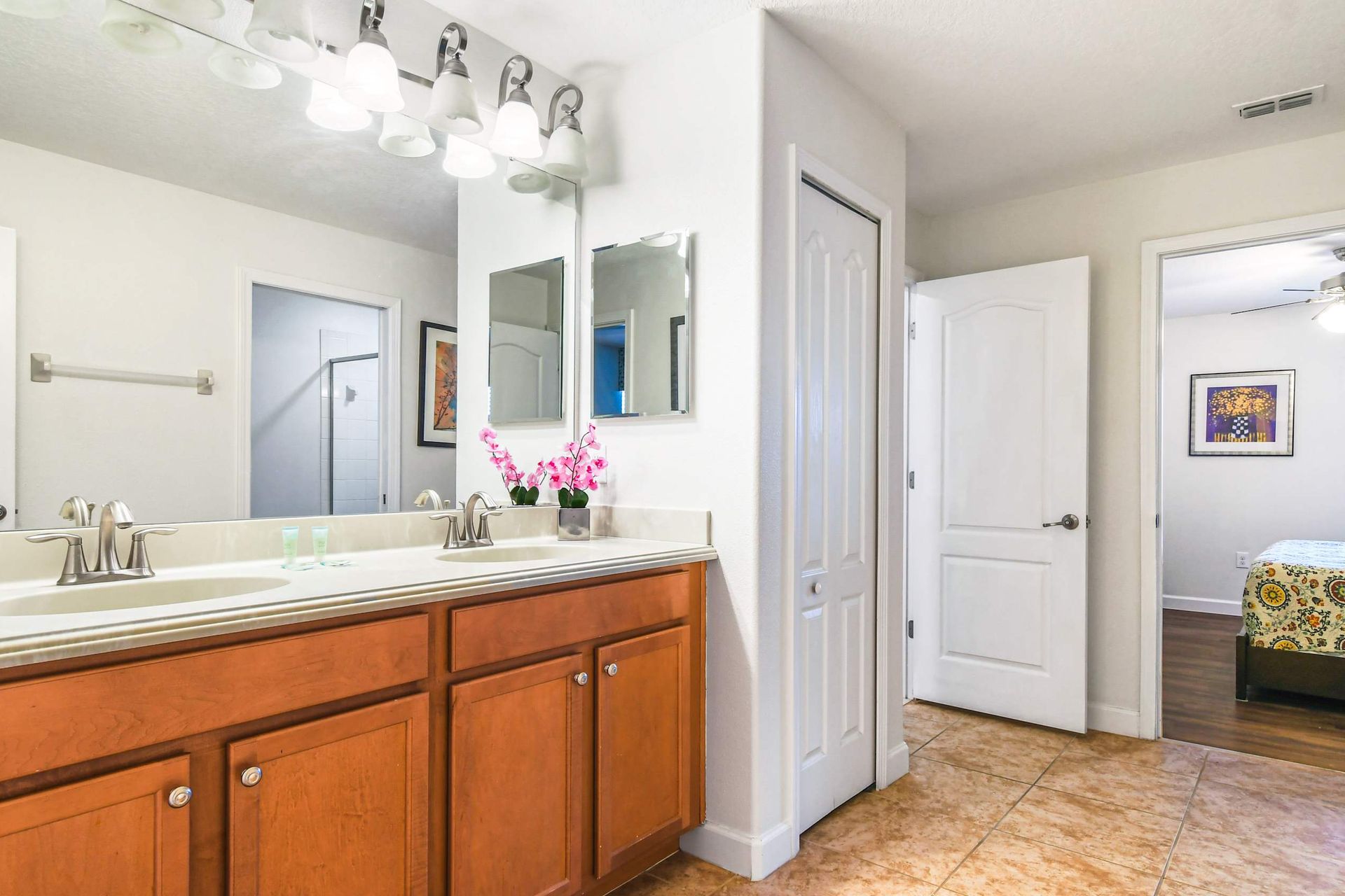 A bright bathroom with a double sink vanity, elegant light fixtures, and decorative orchids for a touch of color.