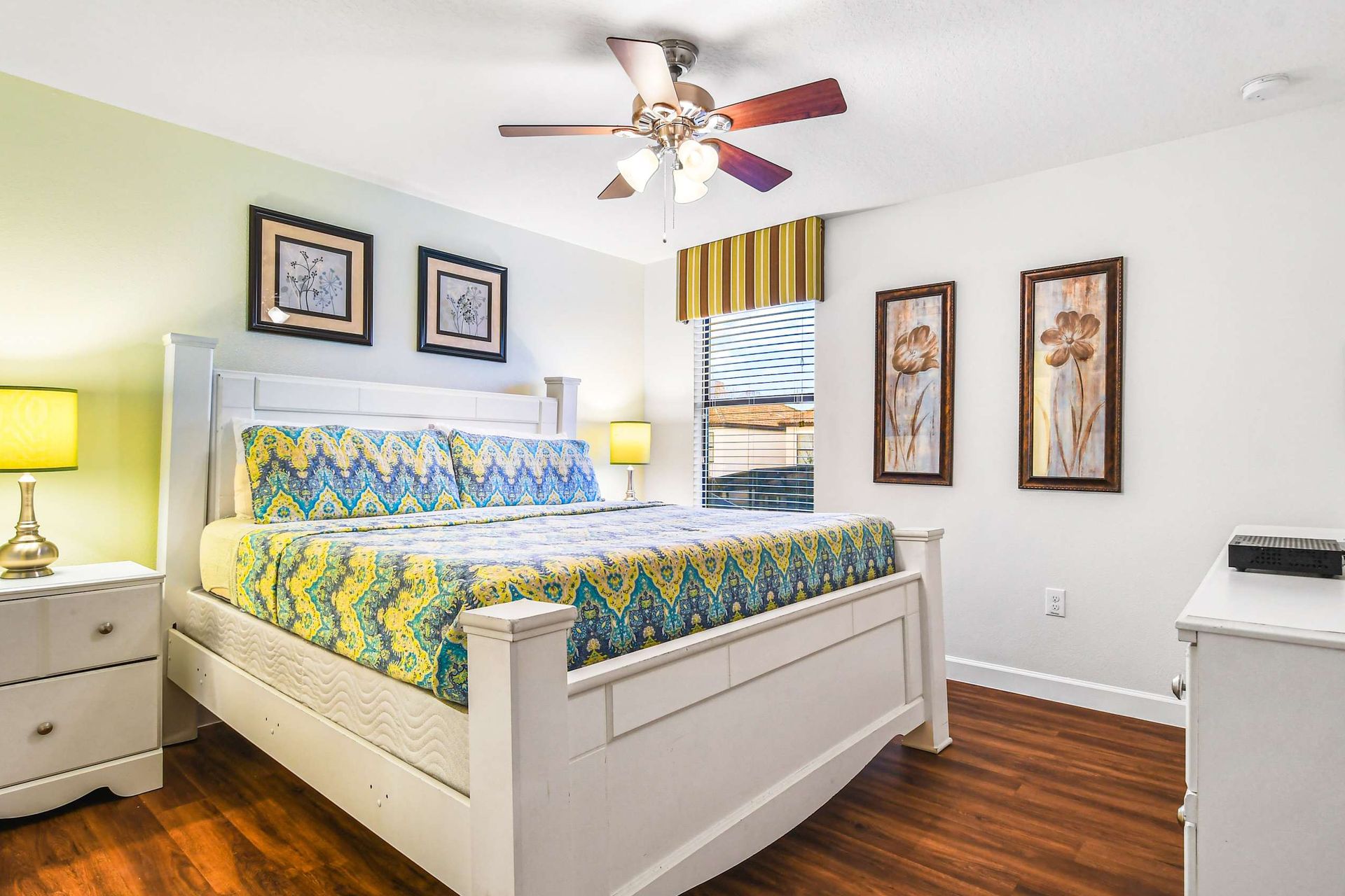 A bright bedroom with a colorful patterned bedspread, white furniture, and warm, inviting decor.