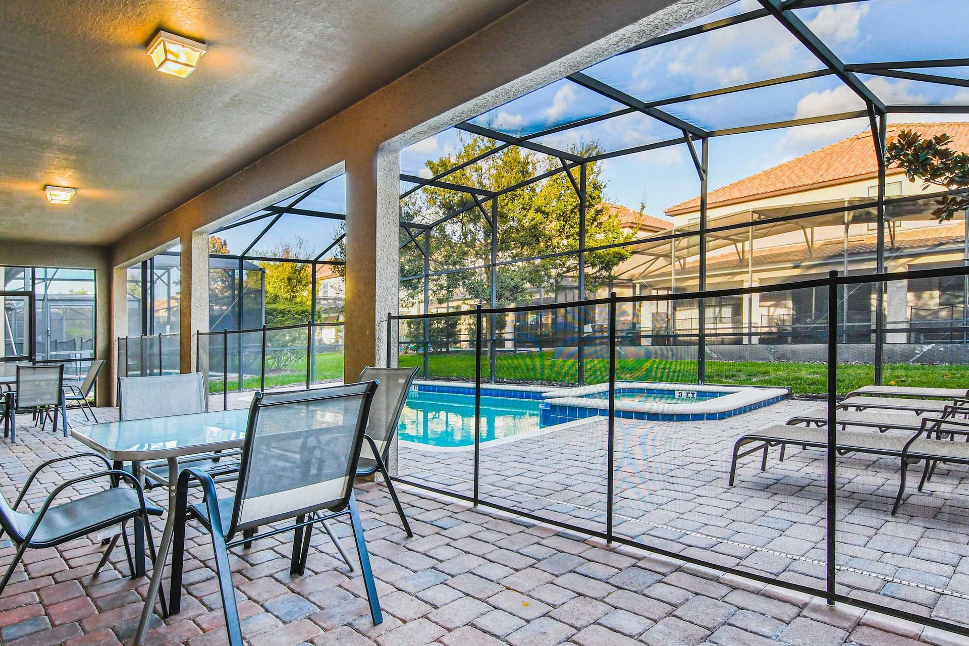 A covered patio with multiple dining sets overlooks a screened-in pool area with lounge chairs and a hot tub.