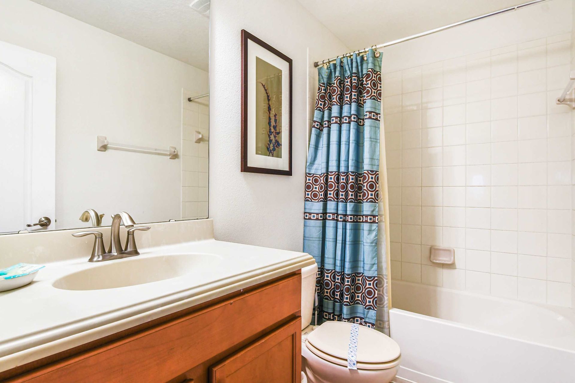 A clean bathroom with a single vanity, bright countertop, framed wall art, and a stylish blue shower curtain.