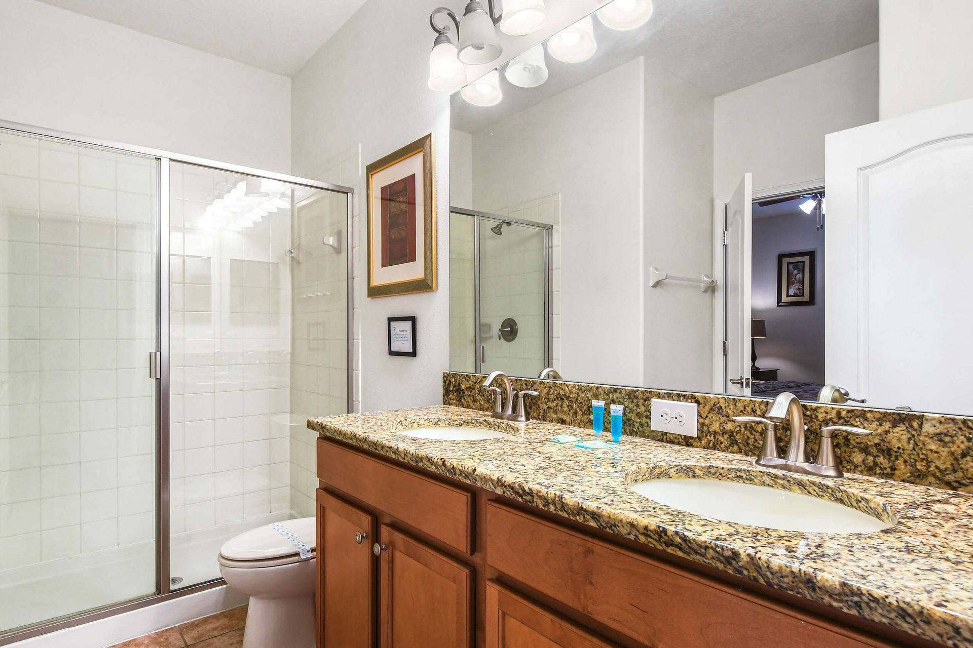 A modern bathroom with a granite double vanity, framed mirror, and a spacious glass-enclosed shower.