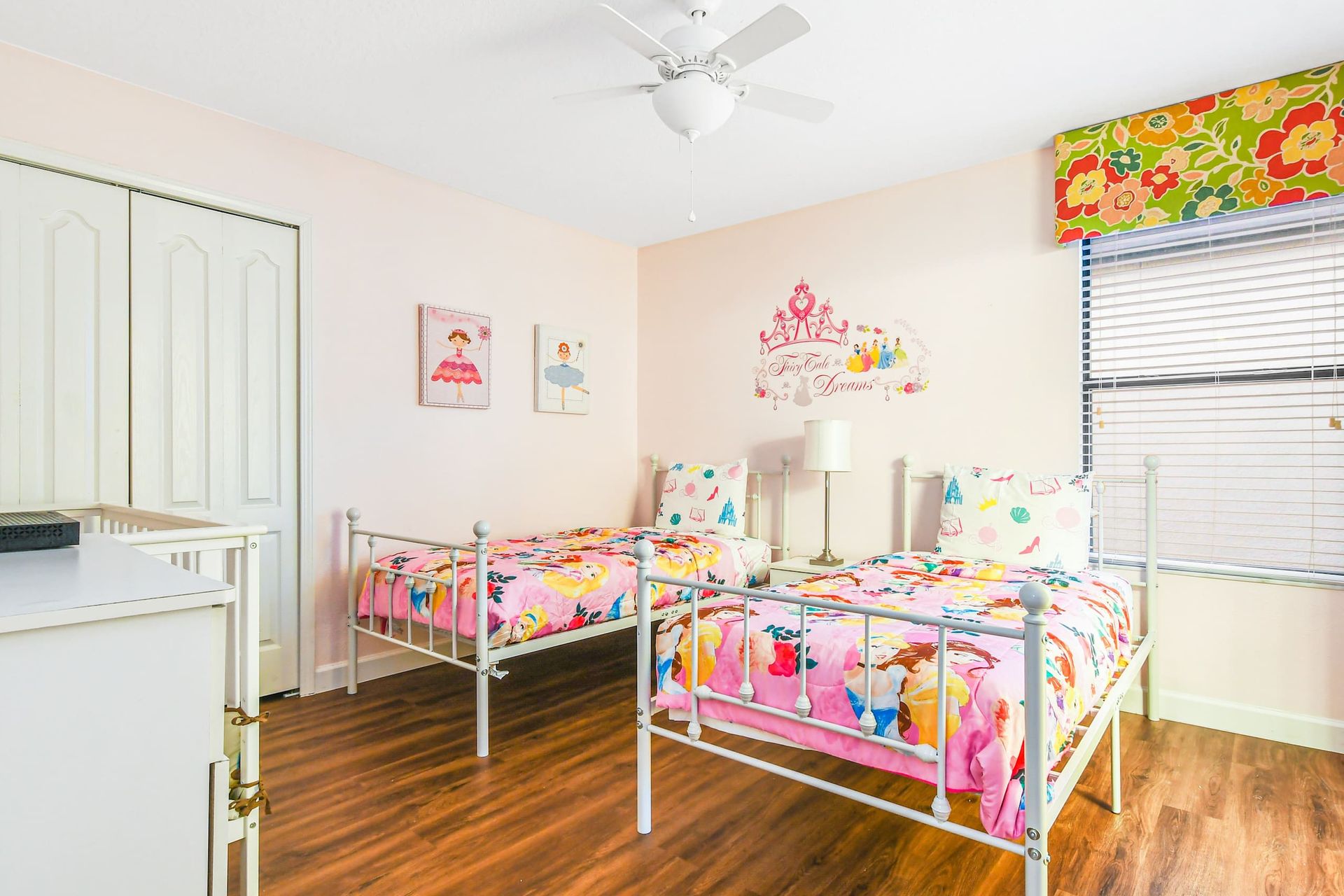 A cheerful children's bedroom with twin beds, vibrant pink bedding, and playful wall art.