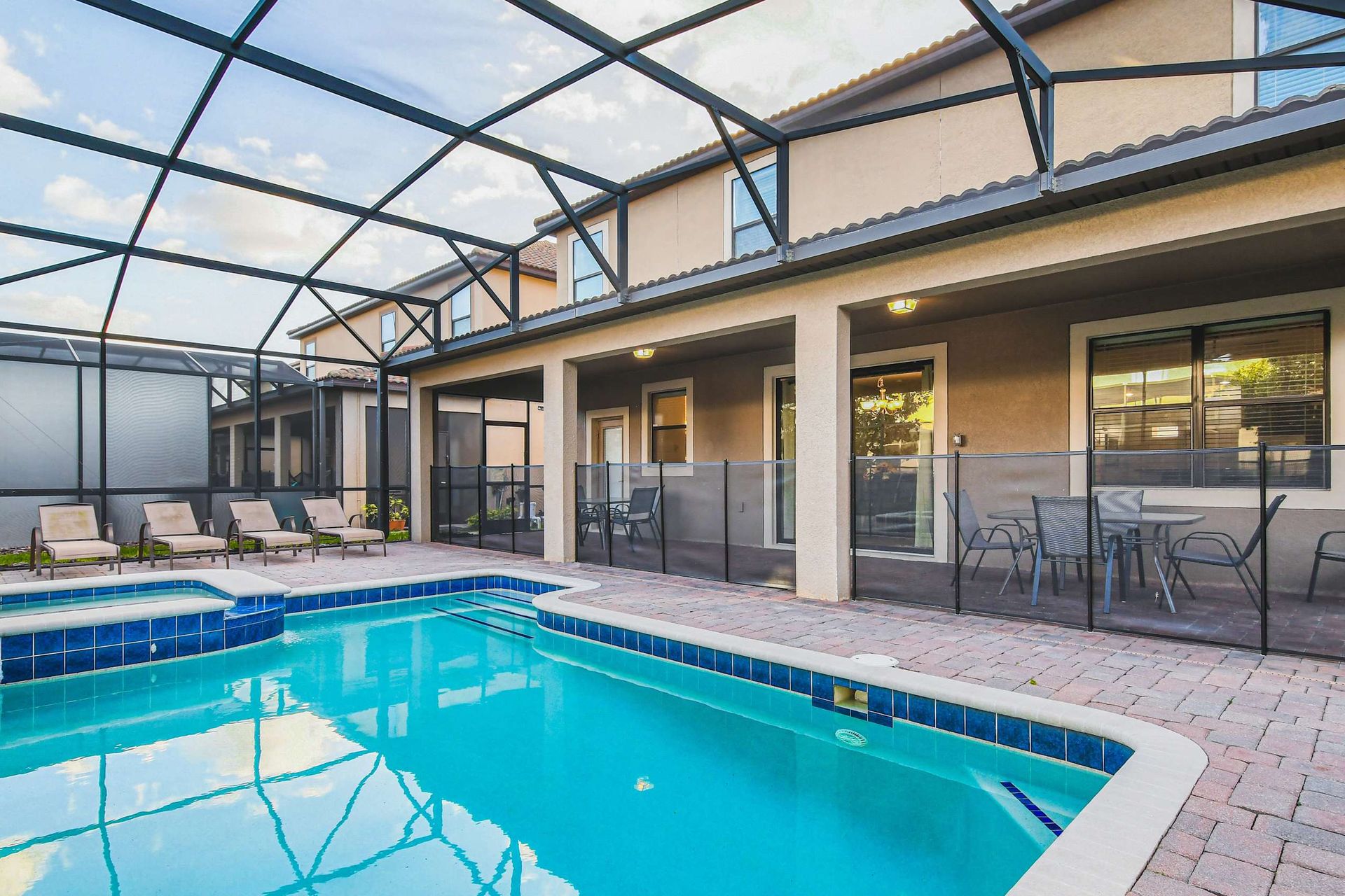 A screened-in backyard with a sparkling pool, hot tub, lounge chairs, and a covered patio dining area.