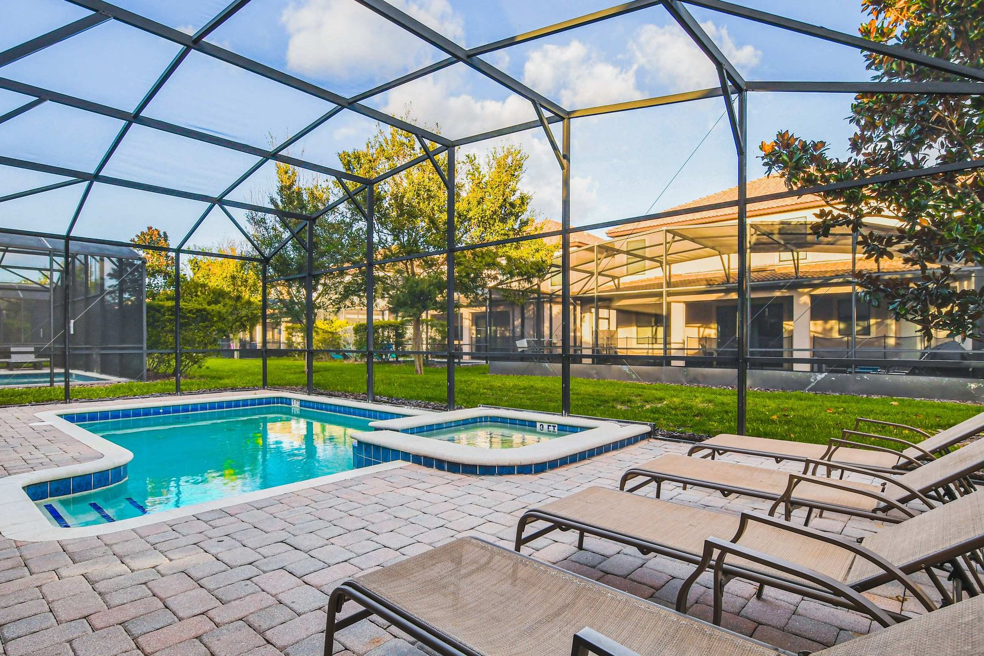 A serene screened-in patio featuring a pool, hot tub, and several lounge chairs, with a view of the lush green yard.