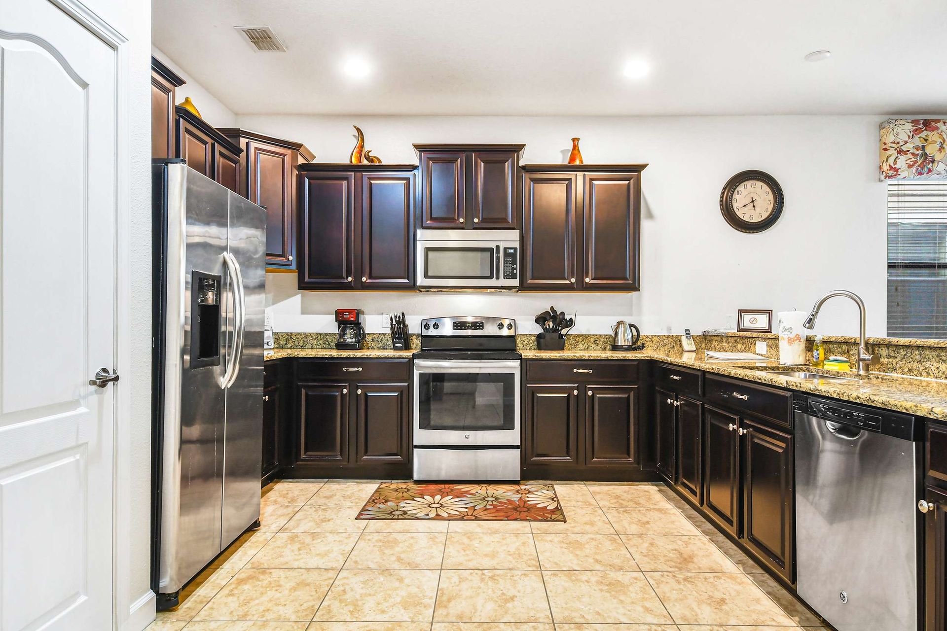 A modern kitchen with dark wood cabinets, granite countertops, stainless steel appliances, and a tiled floor.