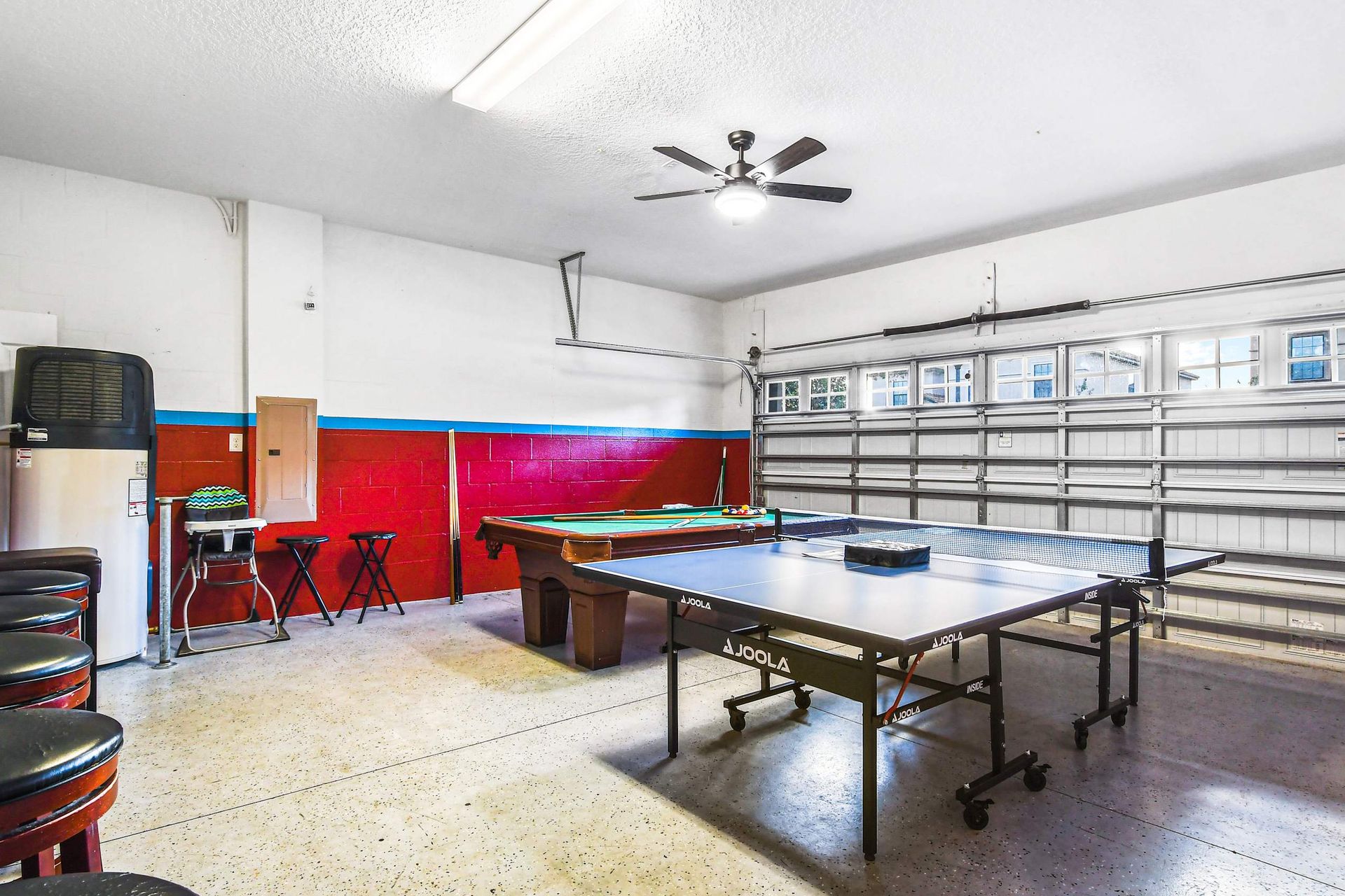 A spacious game room with a ping pong table, pool table, and barstools, set in a clean garage.