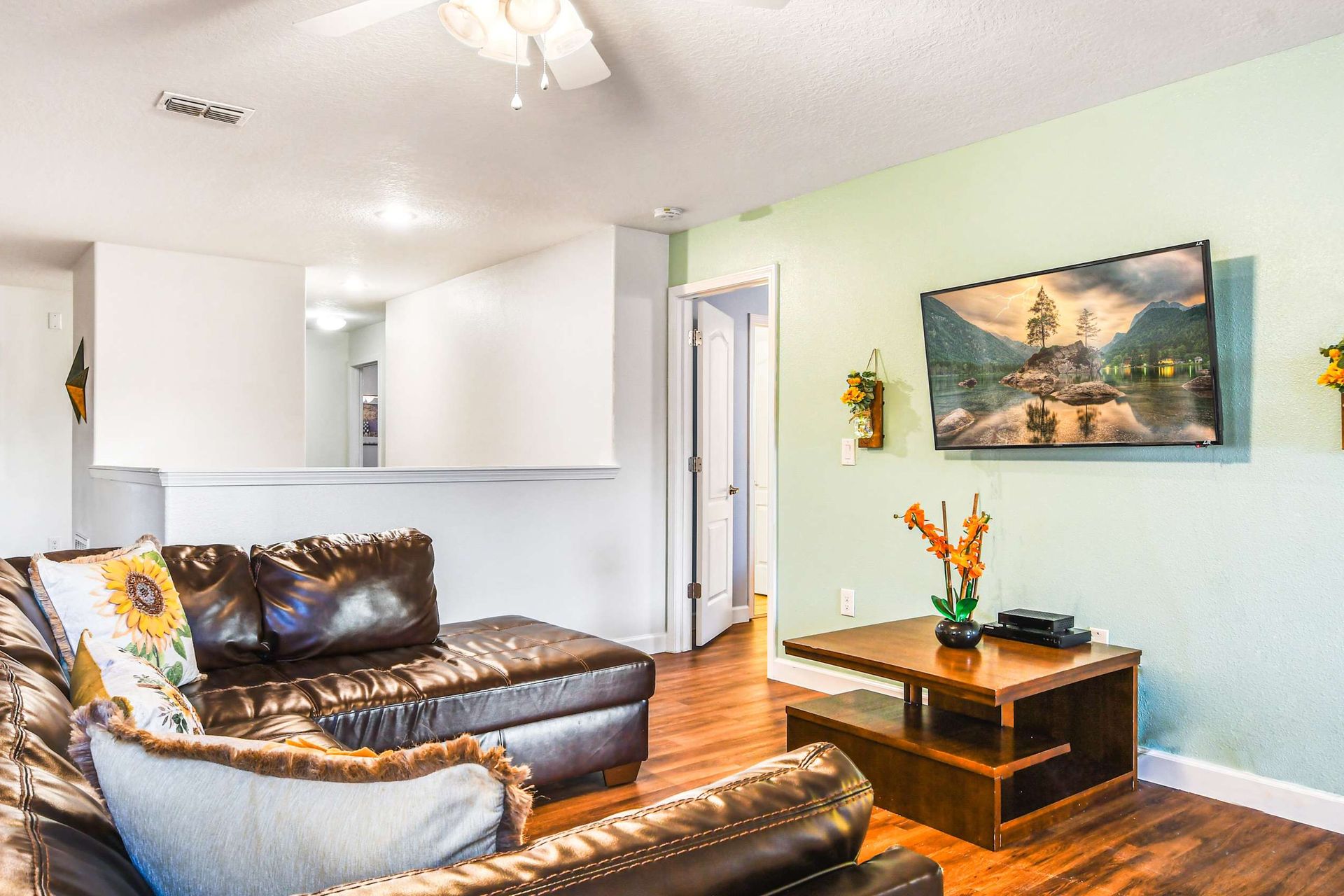 A cozy family room with a leather sectional sofa, vibrant sunflower pillows, and a wall-mounted TV.