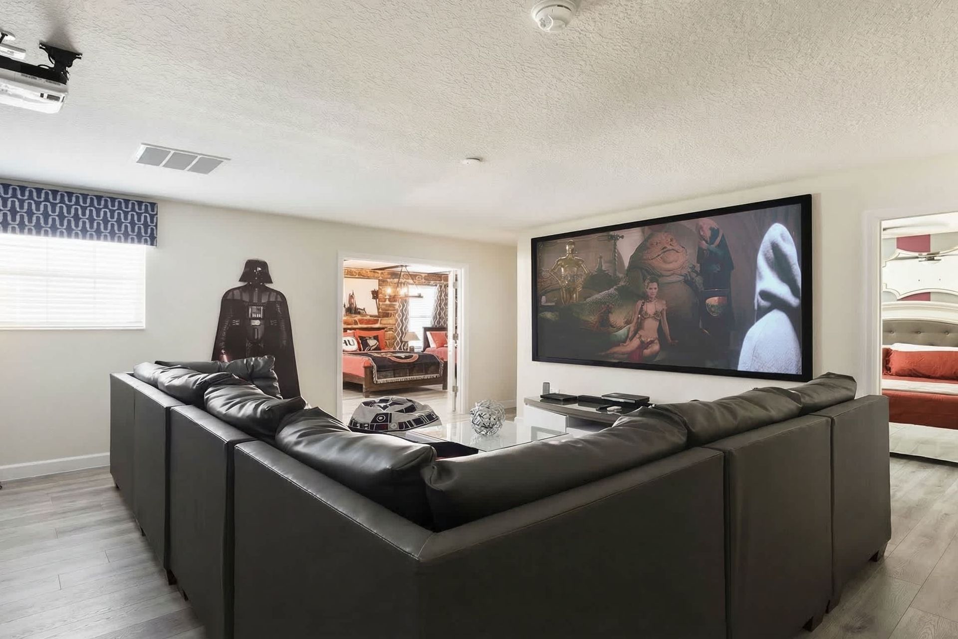 Home theater with a Star Wars theme, featuring a large screen, Darth Vader cutout, and cozy seating.