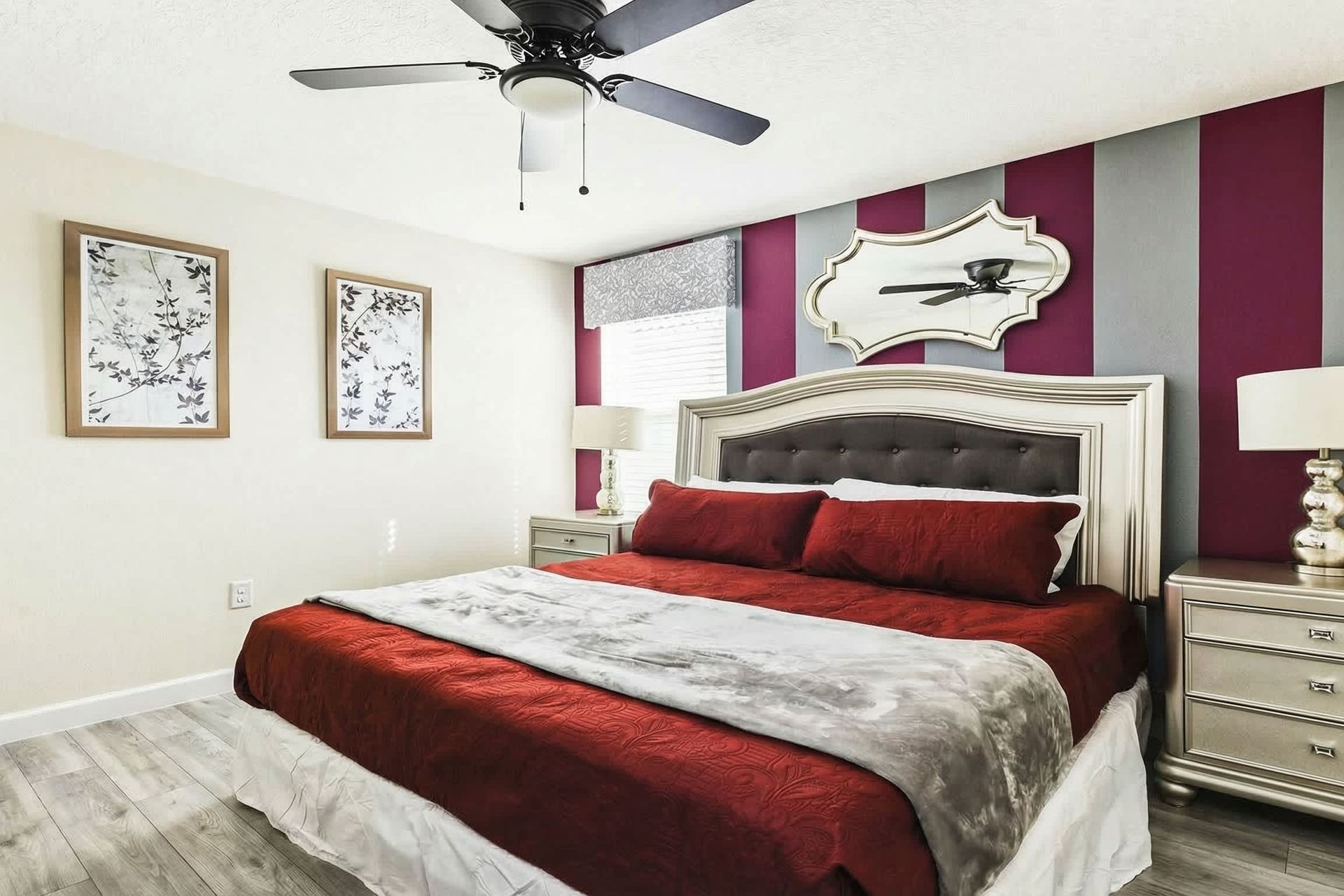 Elegant bedroom with red and gray striped accent wall, luxurious bedding, mirrored decor, and stylish furnishings.