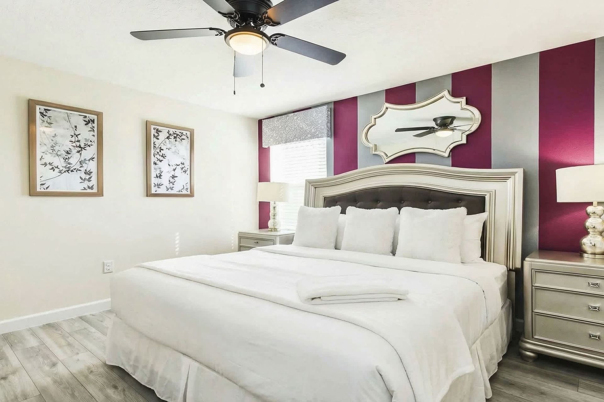 Elegant bedroom with red and gray striped accent wall, luxurious bedding, mirrored decor, and stylish furnishings.
