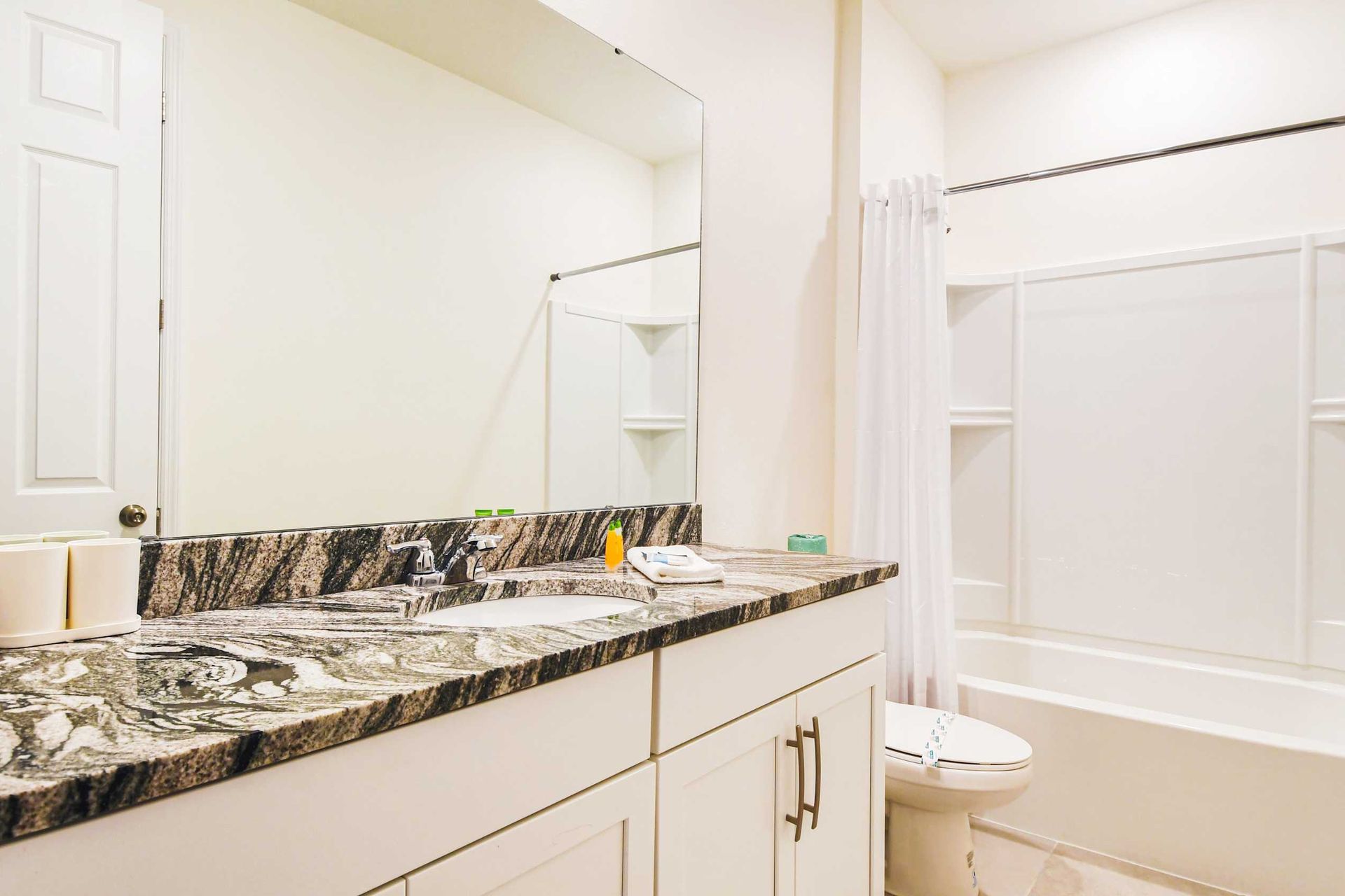 Bright bathroom with granite countertops, large mirror, and a clean tub/shower.