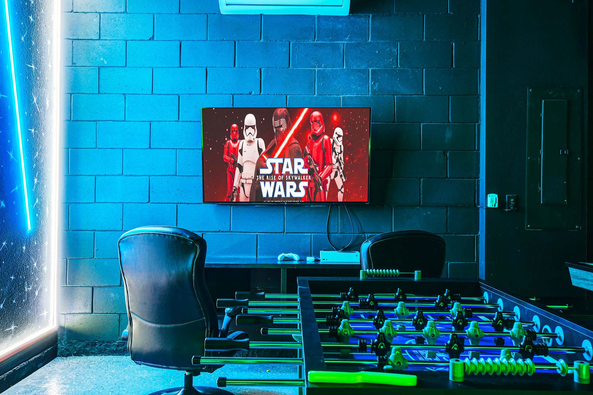 Sci-fi themed game room with foosball, gaming setup, and vibrant neon lighting.