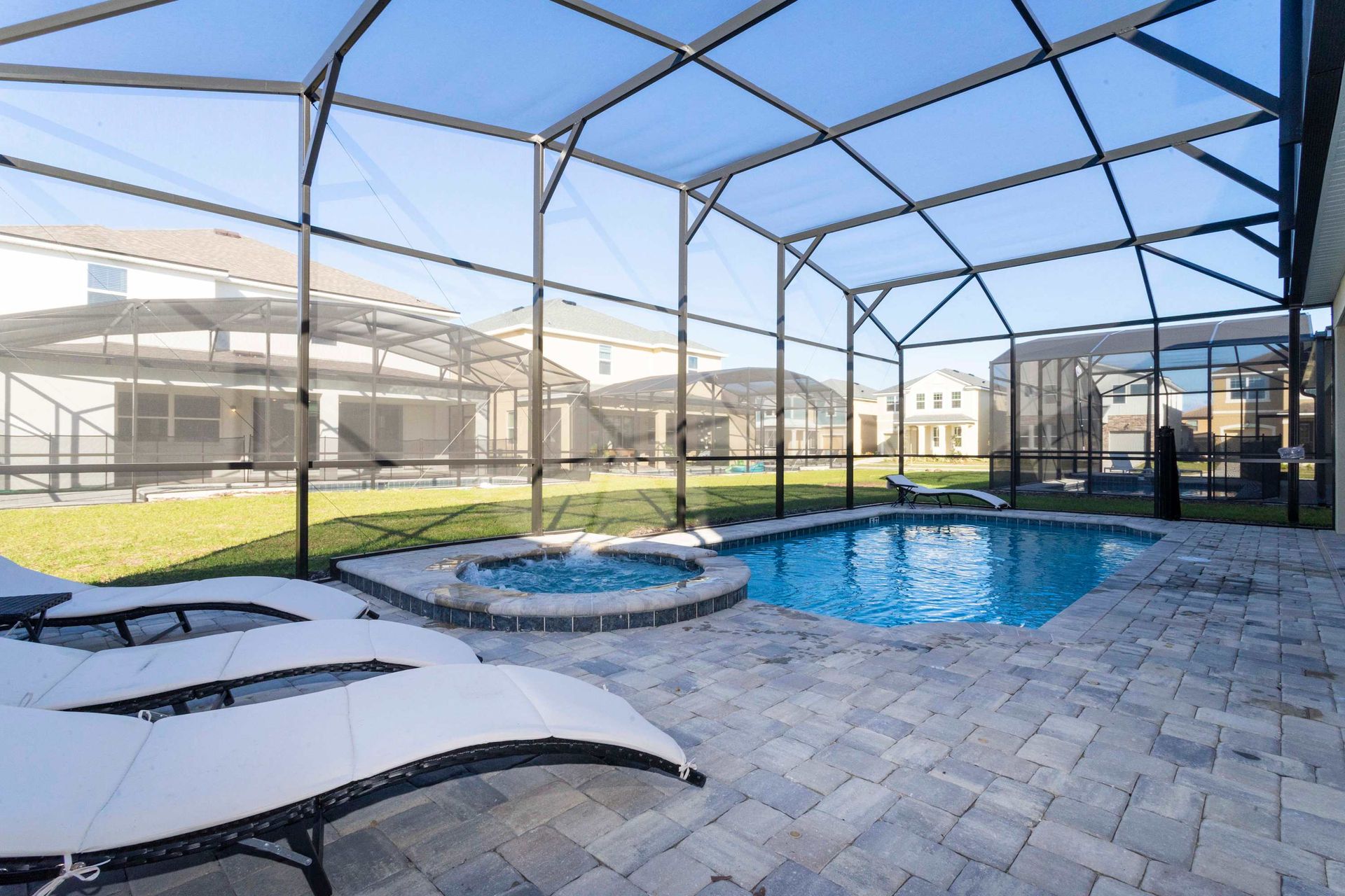 Sunny private pool area with spa, lounge chairs, and screened-in enclosure.