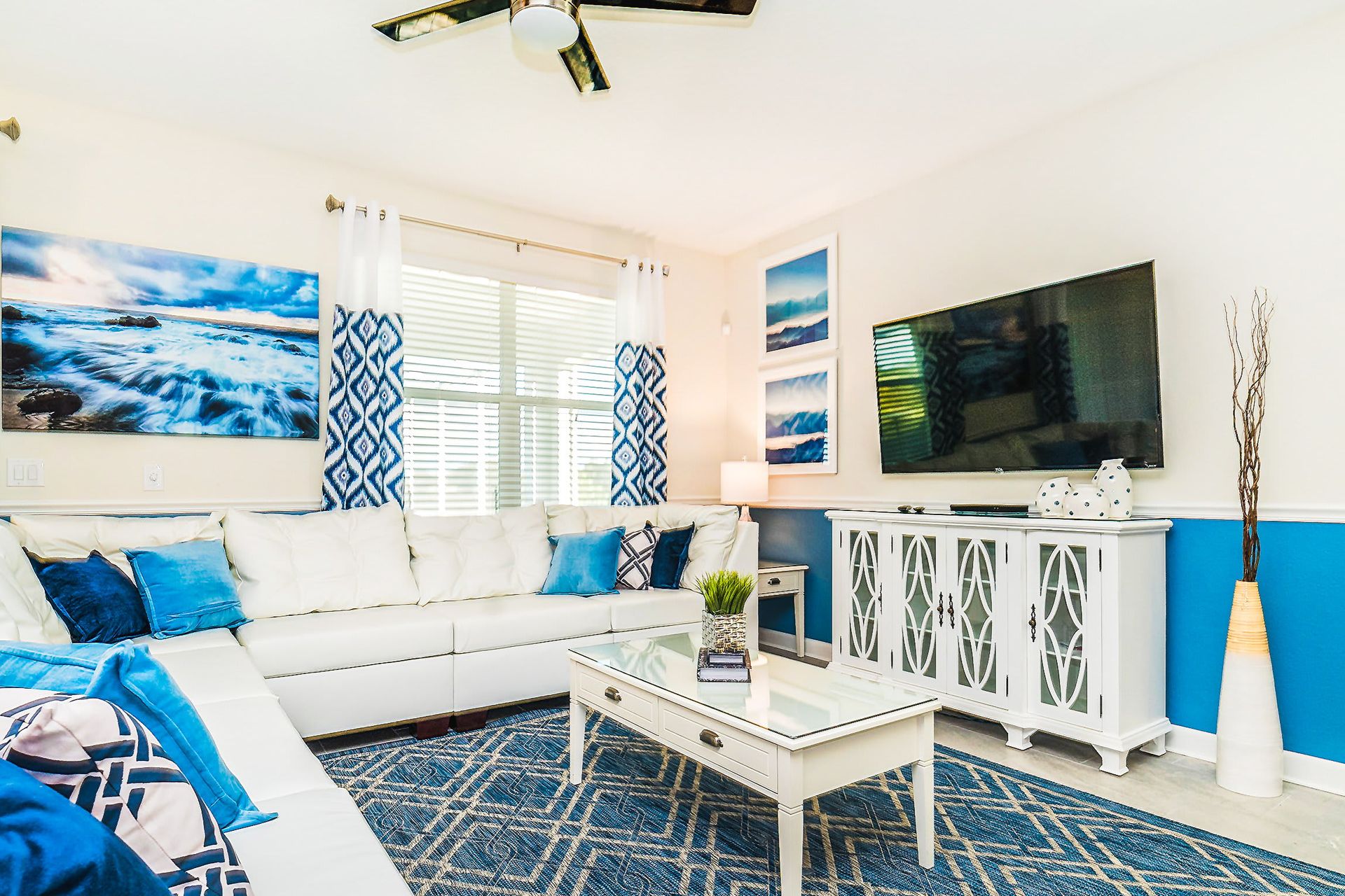 Bright coastal-themed living room with a white sectional sofa, blue accents, and a large TV.