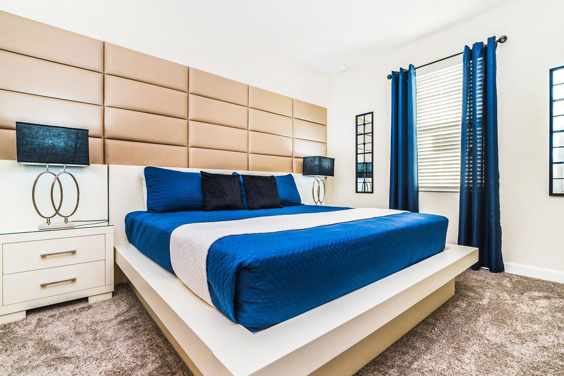 Modern bedroom with a platform king bed, padded headboard, and sleek decor in blue and beige tones.