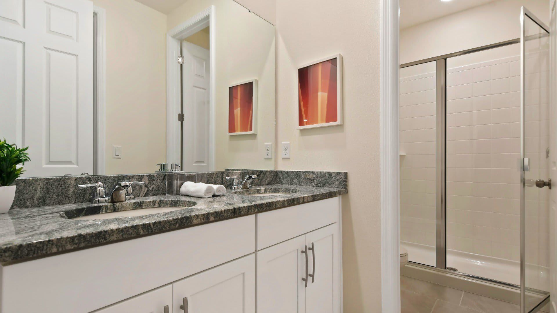 Modern bathroom with dual sinks, granite countertops, and a spacious glass-enclosed shower.